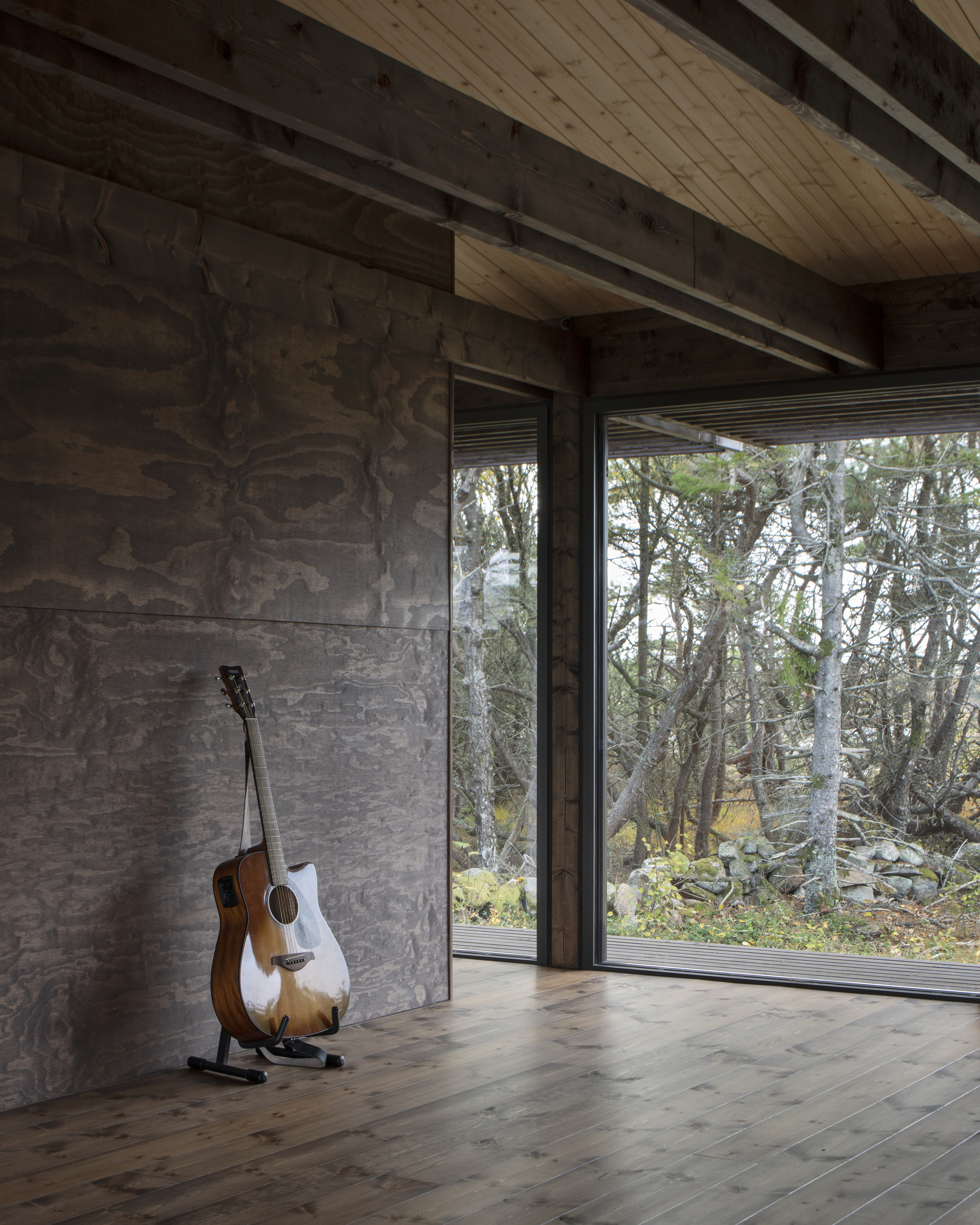 Corner of room with acoustic guitar leaning against marbled plywood wall beside glazed door to landscape