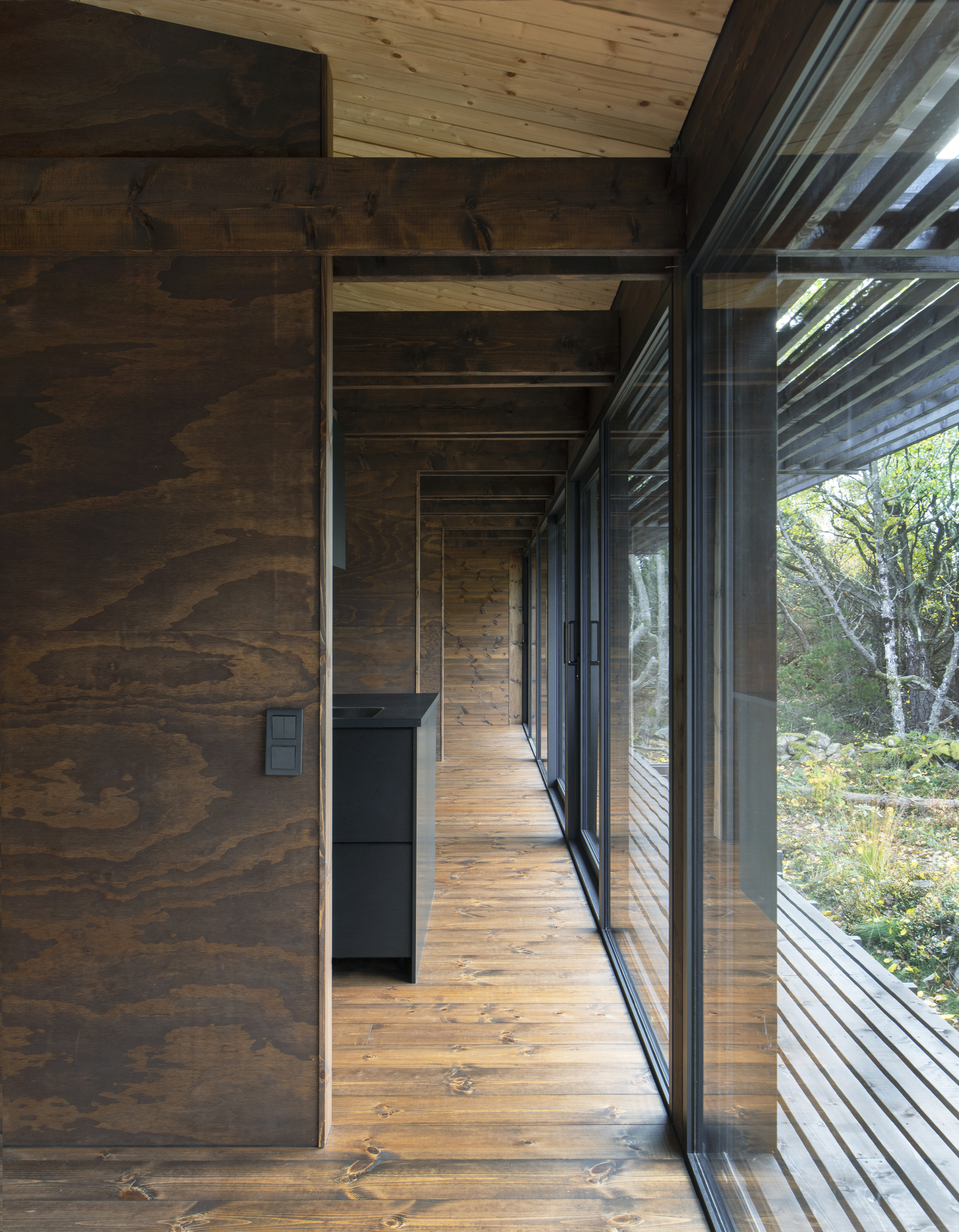 Timber corridor with wood slat ceiling and continuous glazing along one side opening to trees