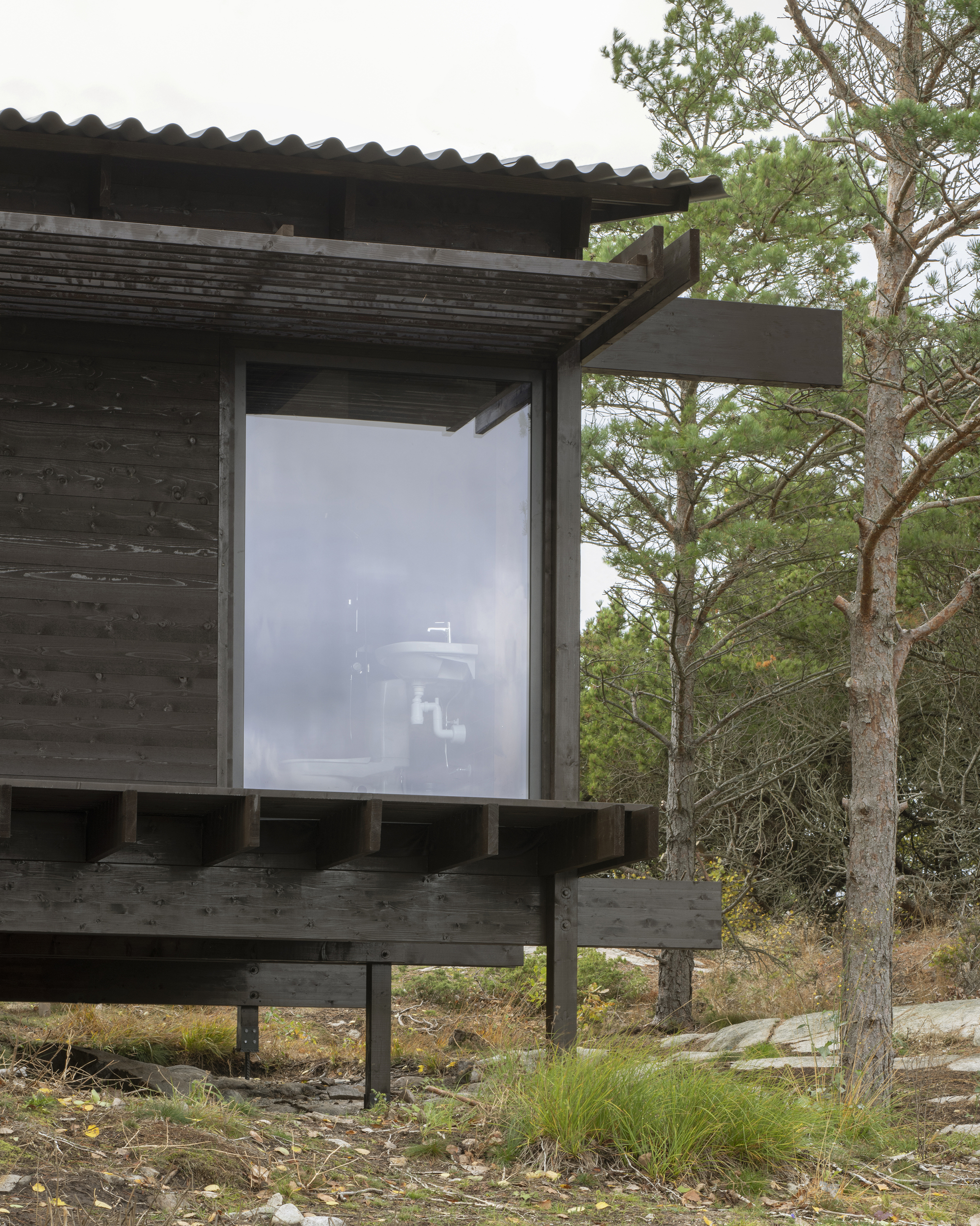 Corner window detail with blackened timber cladding and deep overhang supported by exposed timber posts