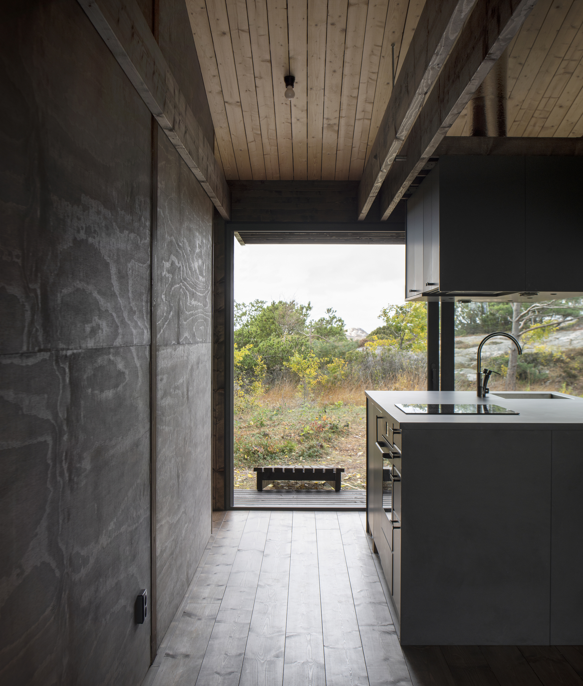 Kitchen interior with concrete cabinet walls and wood plank ceiling opening to landscape beyond
