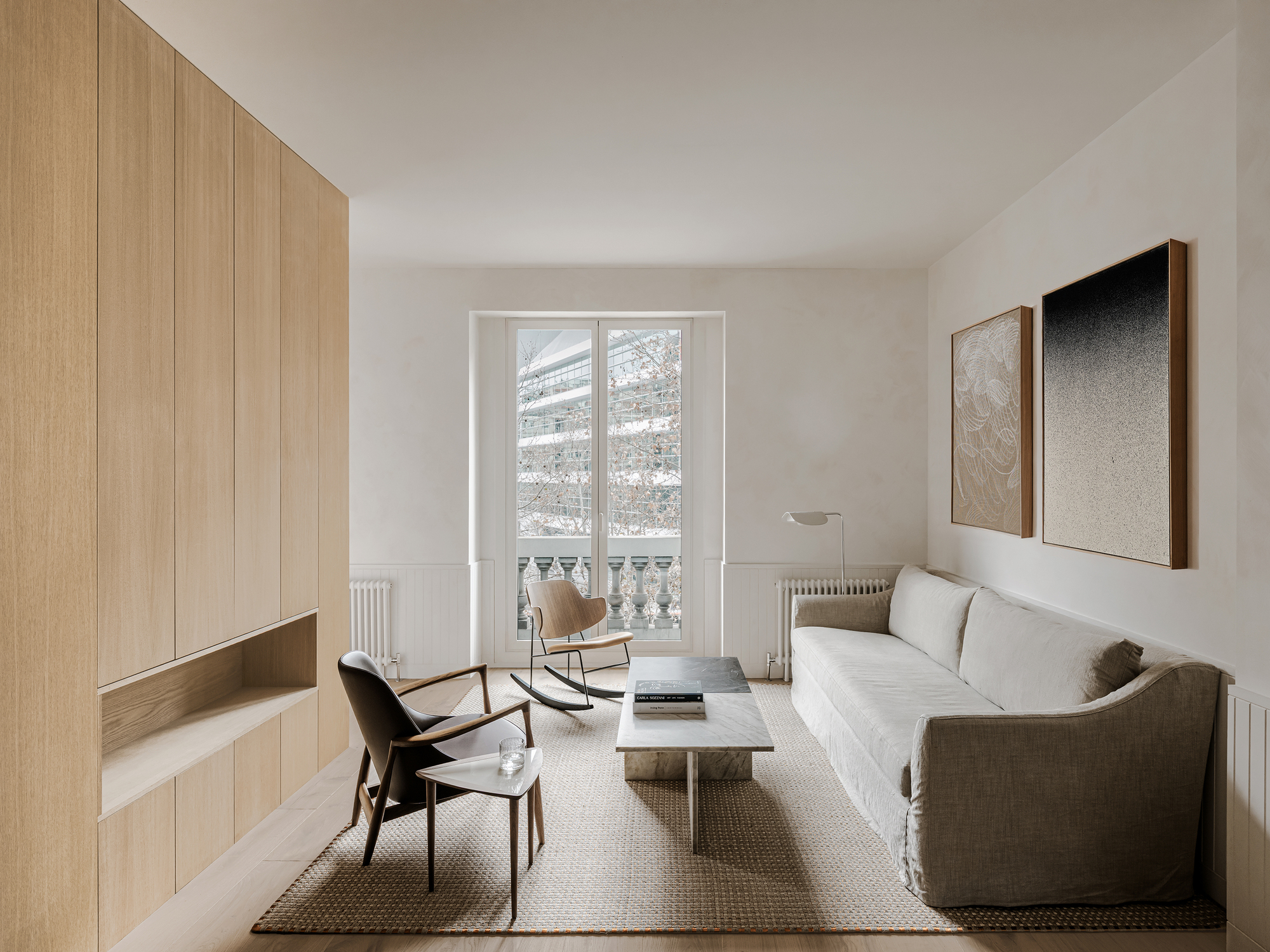 Living room with tall window overlooking winter street, light timber joinery and textured rug