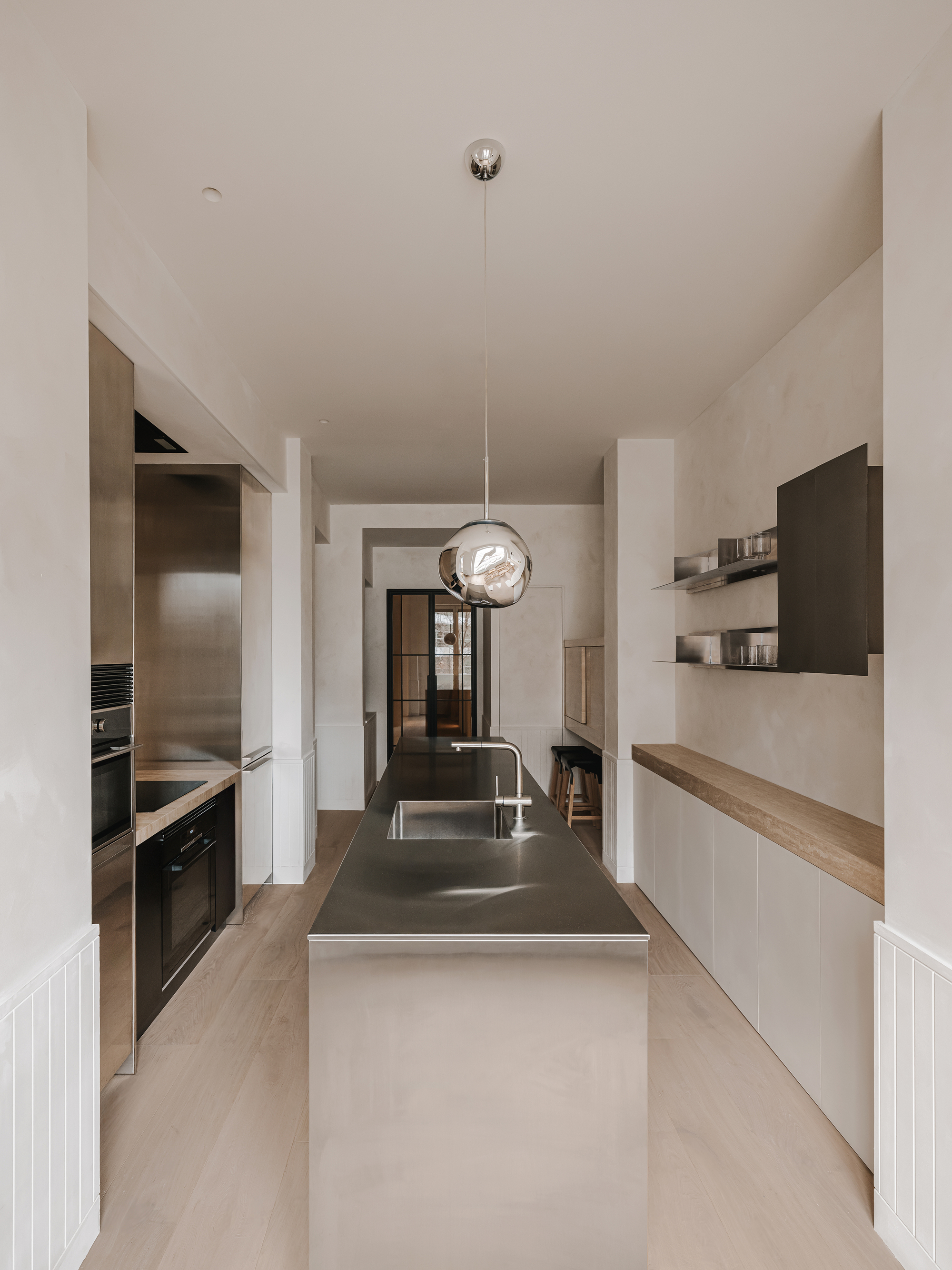 Galley kitchen with stainless steel island, glass pendant and view through to glazed doors