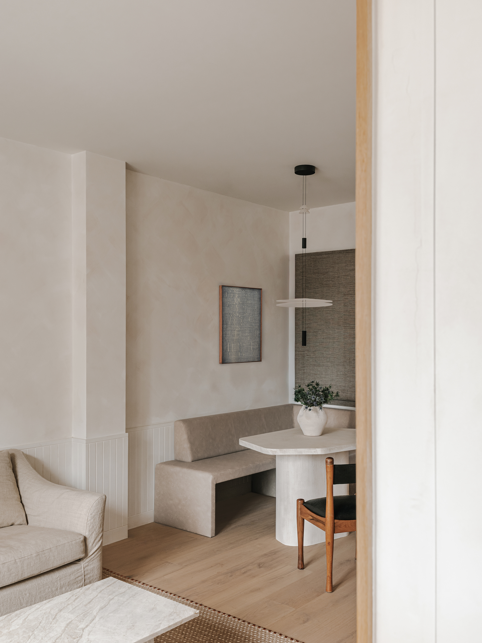 Framed view into dining nook with built-in seating and cylindrical table beneath pendant light