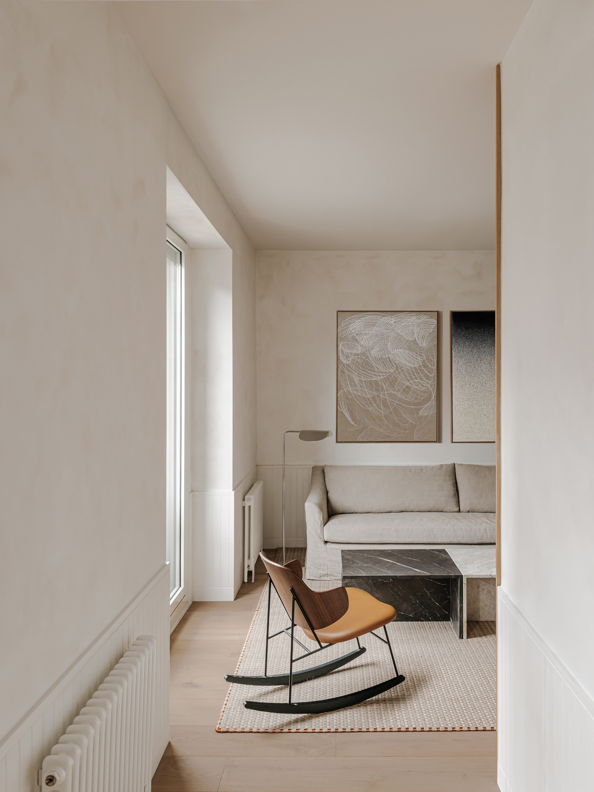 Living room with pale timber flooring, tall window, and leather rocking chair on a cream rug
