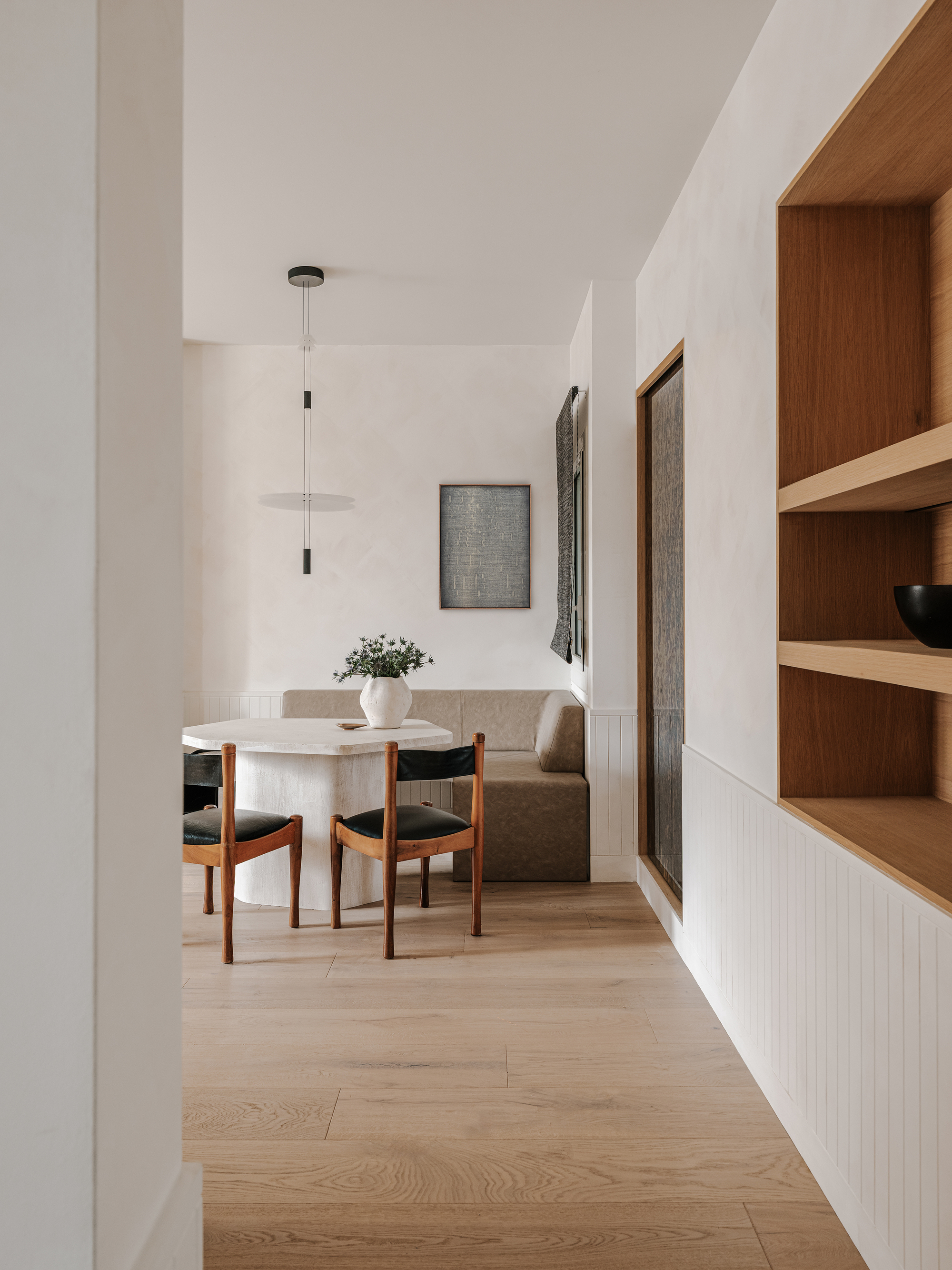 Dining nook with built-in bench, round table, and timber shelving along the white paneled wall