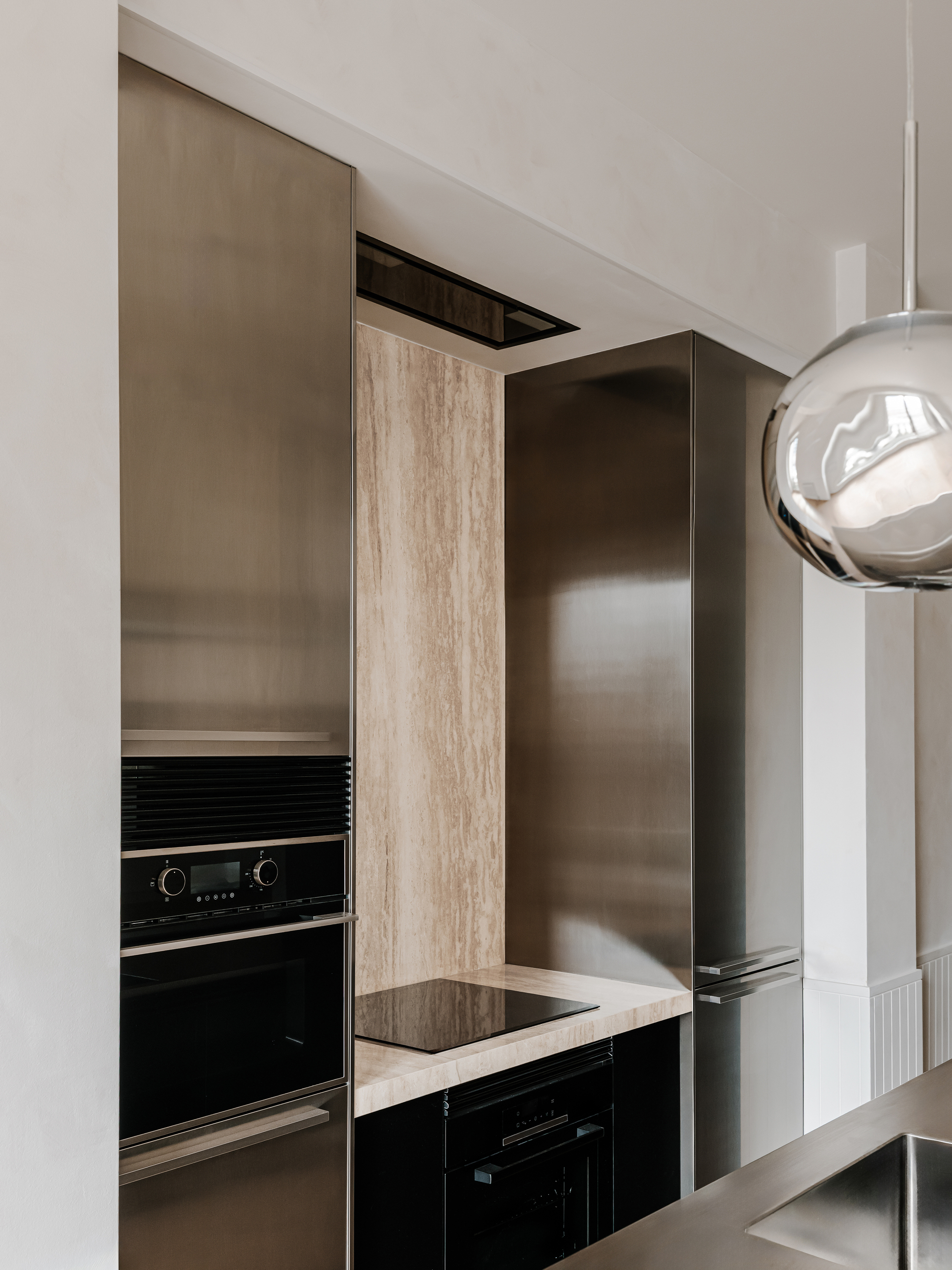 Corner detail of kitchen cabinetry showing brushed metal panels meeting timber veneer and black appliances