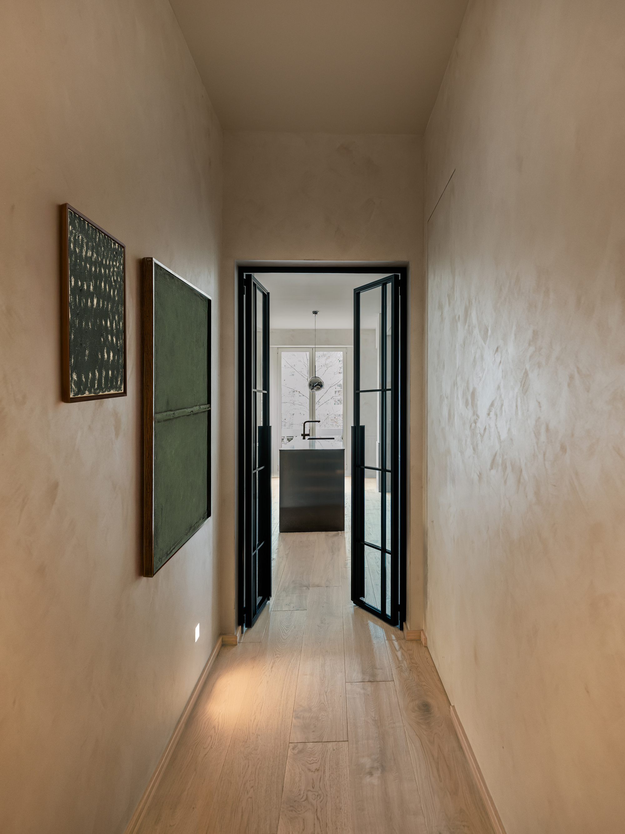 Narrow corridor with limewashed plaster walls leading to the kitchen through black-framed glass doors