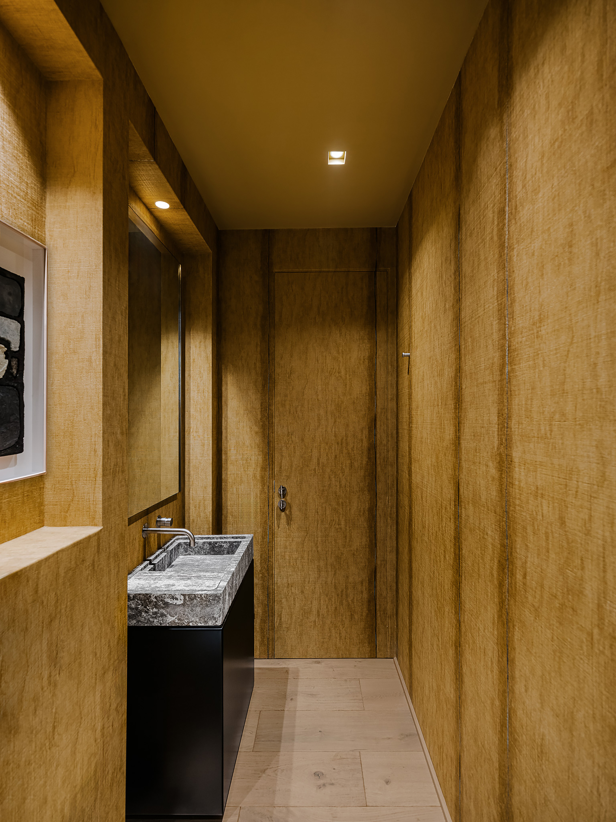 Narrow corridor with vertical wood paneling, marble sink, and recessed ceiling lights