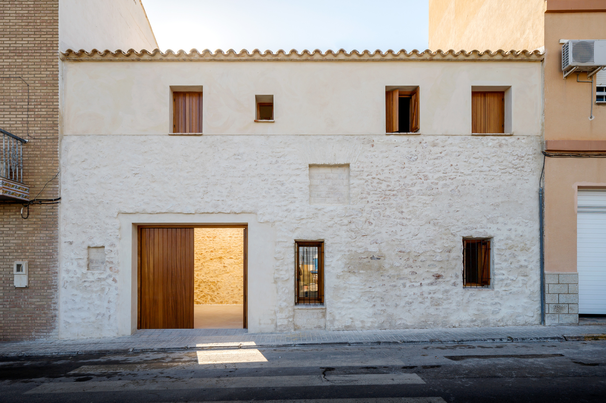 Street view of the white stucco facade with timber-framed openings and terracotta tile roof at dusk
