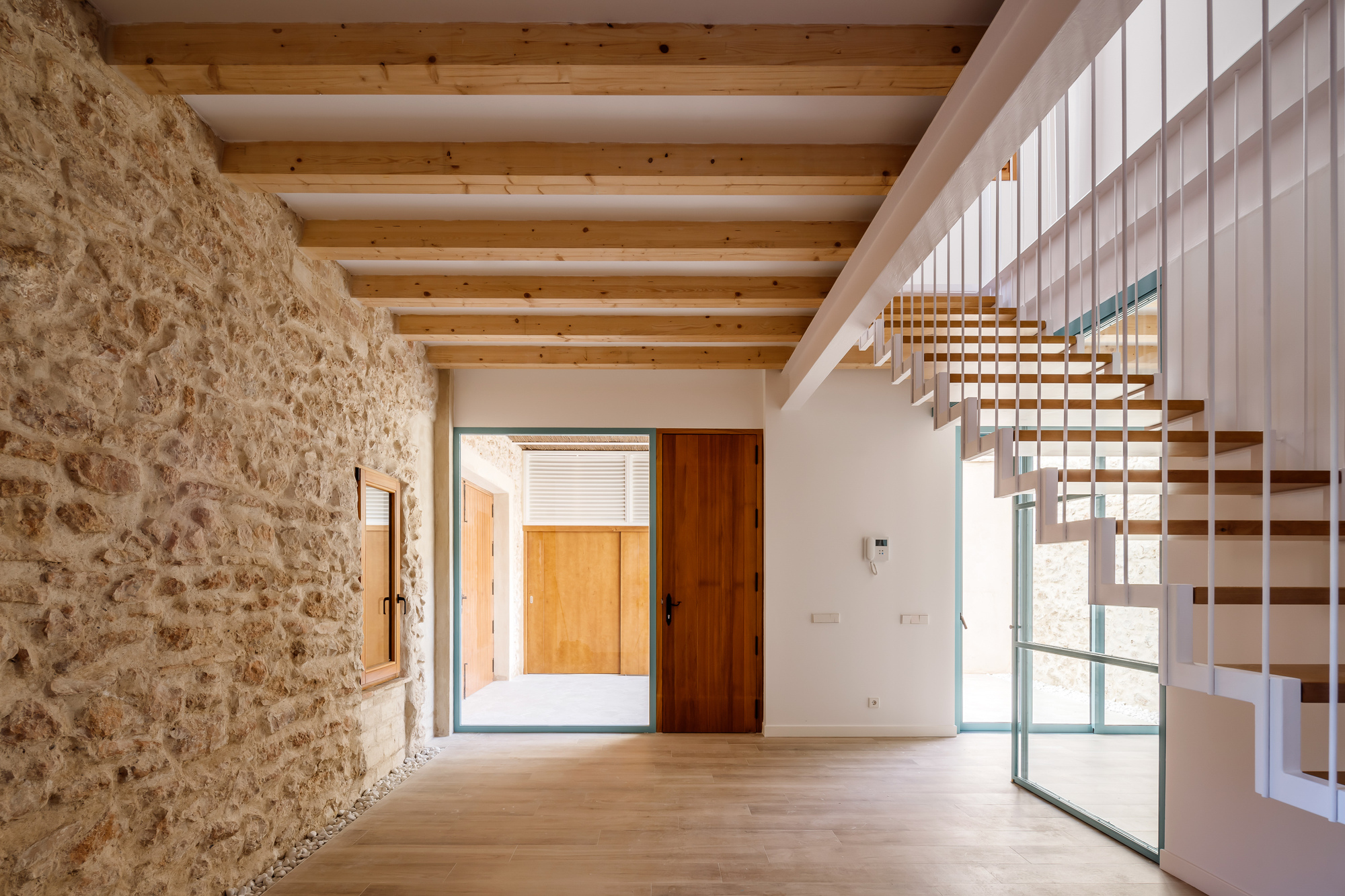 Entry hall with exposed stone wall, timber ceiling beams, and floating wooden staircase beside glazed door