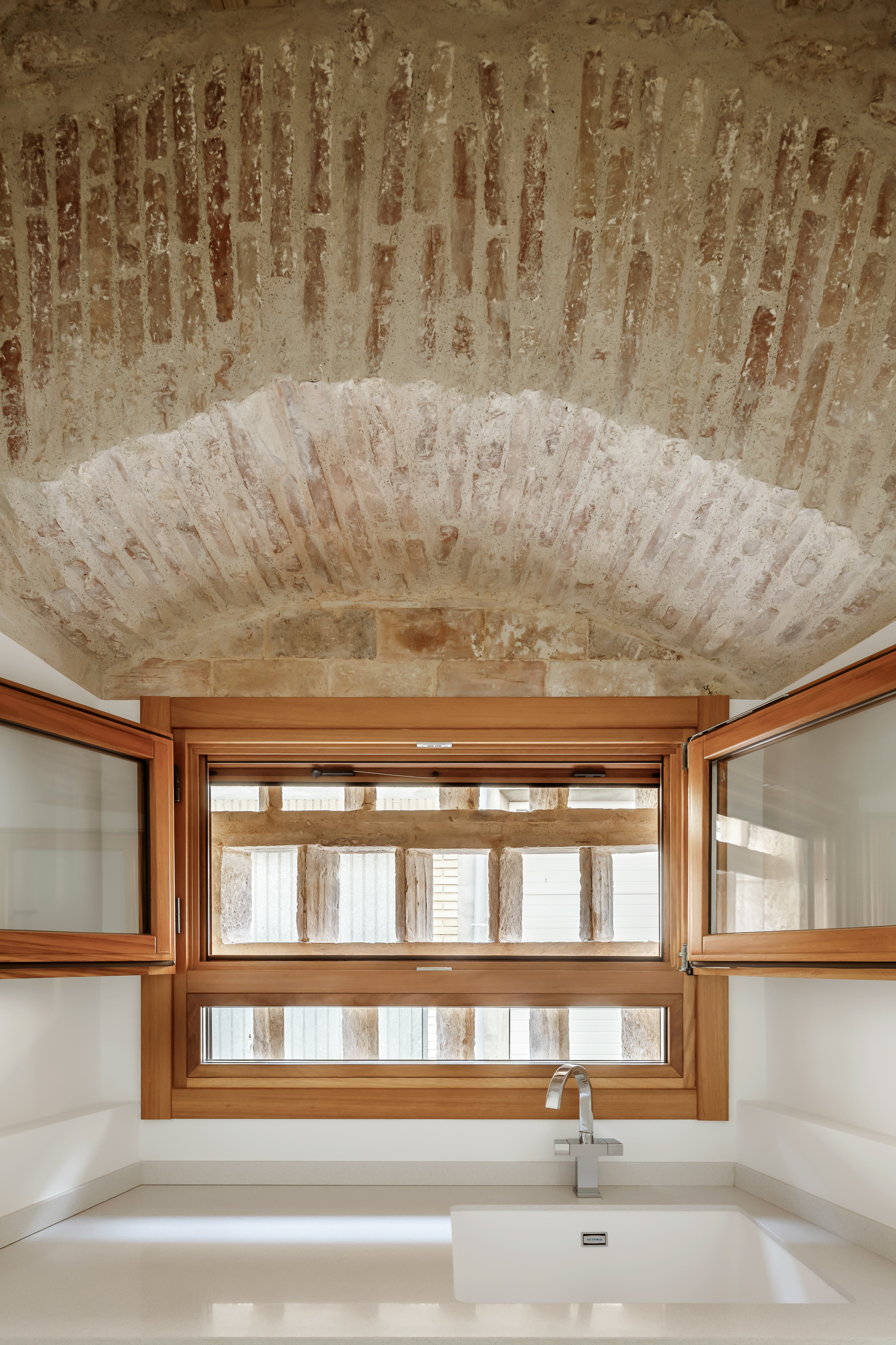 Bathroom with exposed brick vault ceiling above timber-framed horizontal window overlooking the courtyard