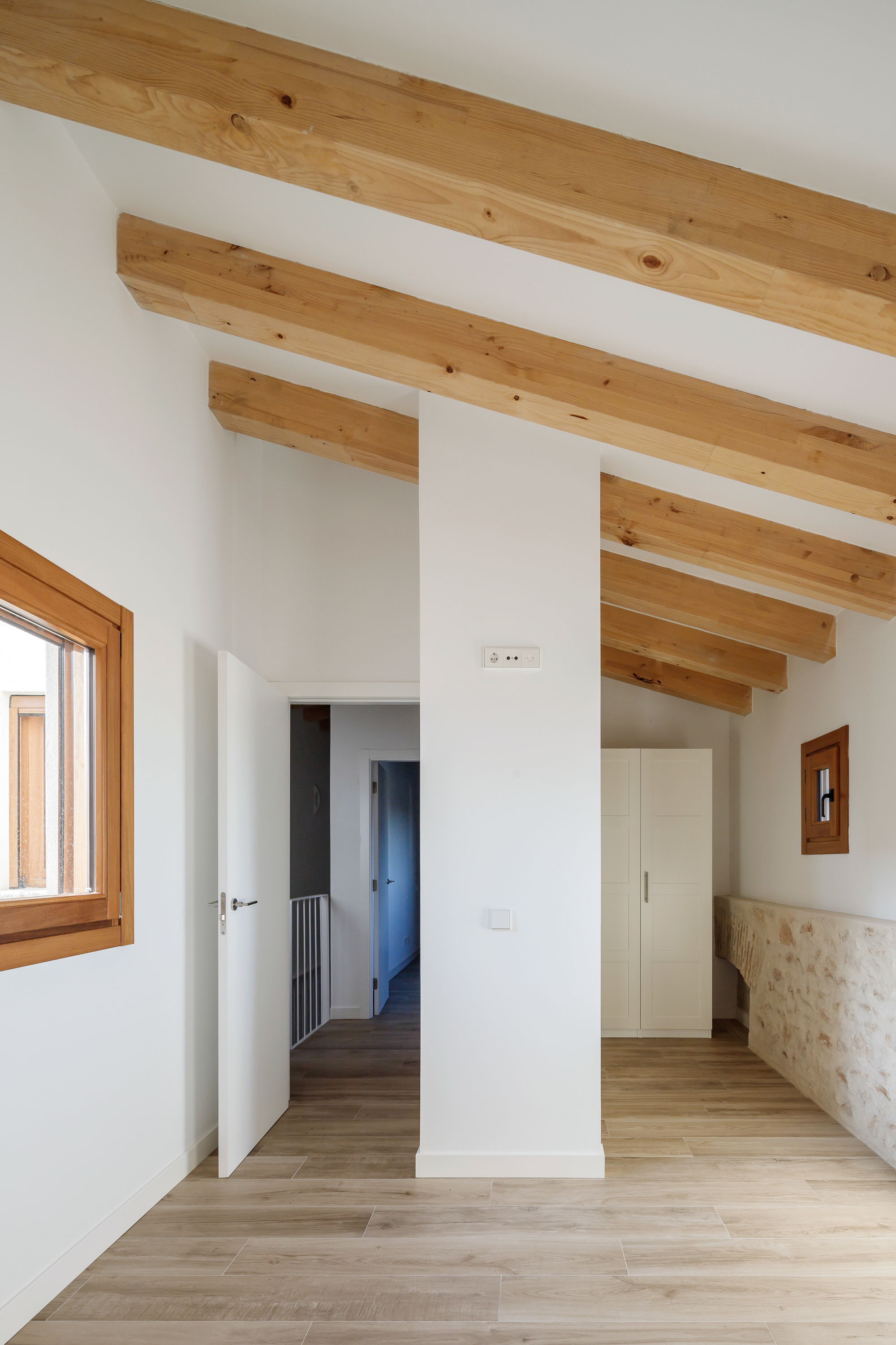 Interior hallway with exposed timber beams crossing white ceiling above light wood floor and doorways
