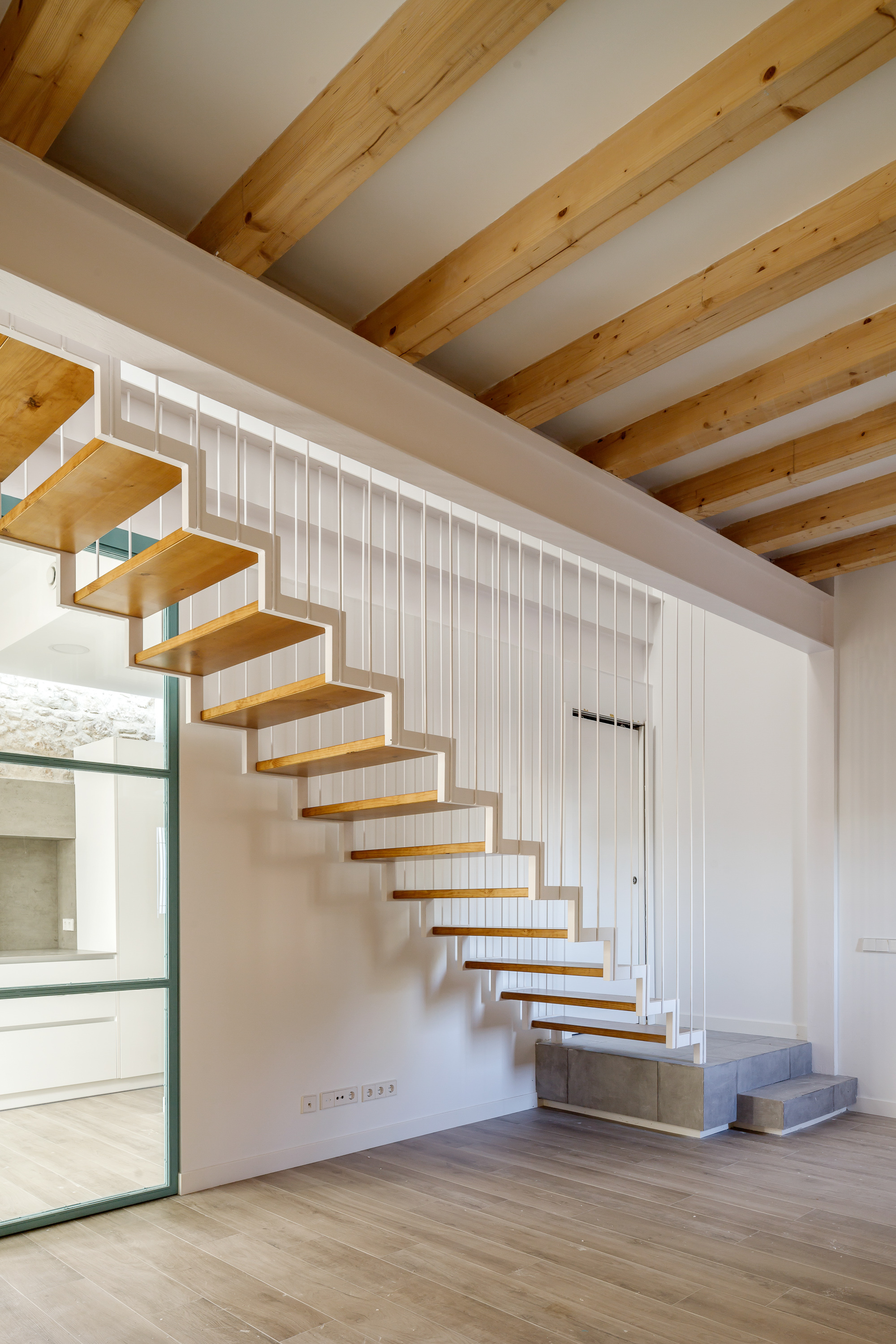 Cantilevered timber staircase with open risers against a white vertical-paneled wall