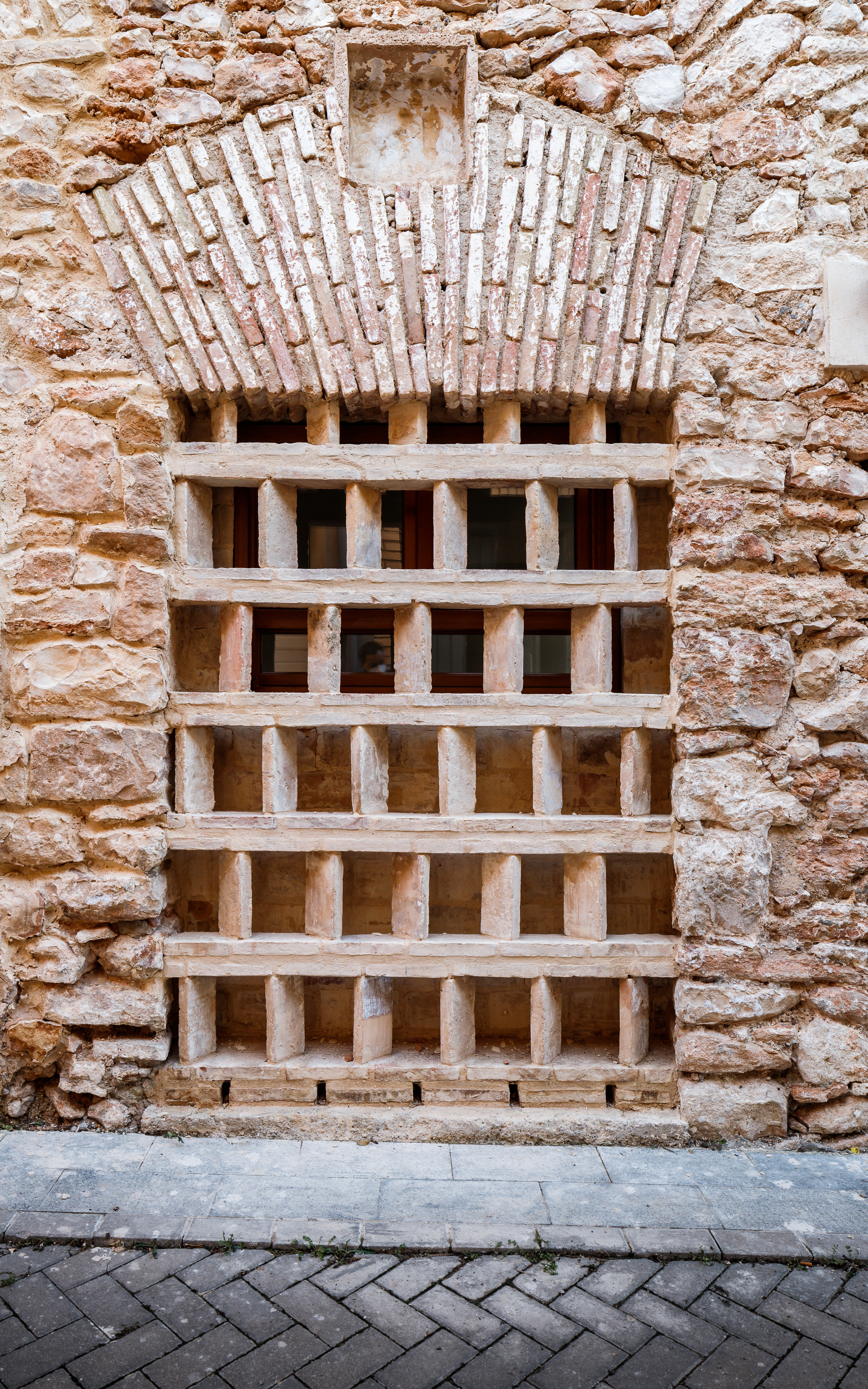 Timber gridded door set within a weathered stone wall above herringbone paving