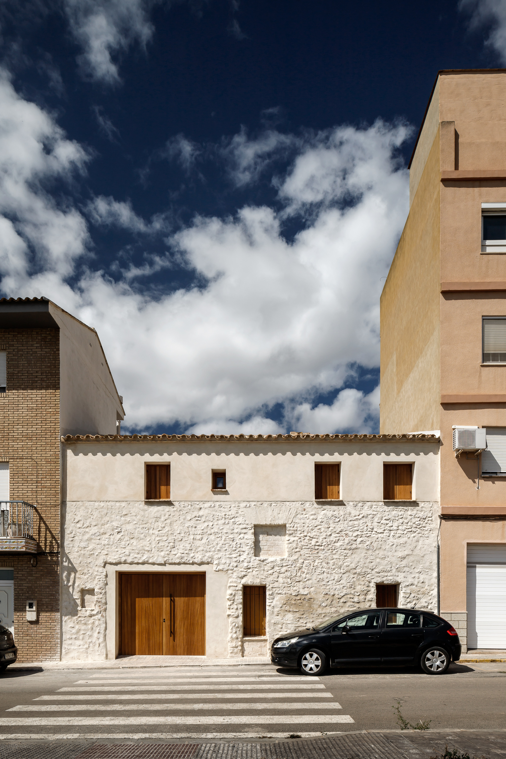 Street view of the white stone facade with timber garage door and a parked car at the curb
