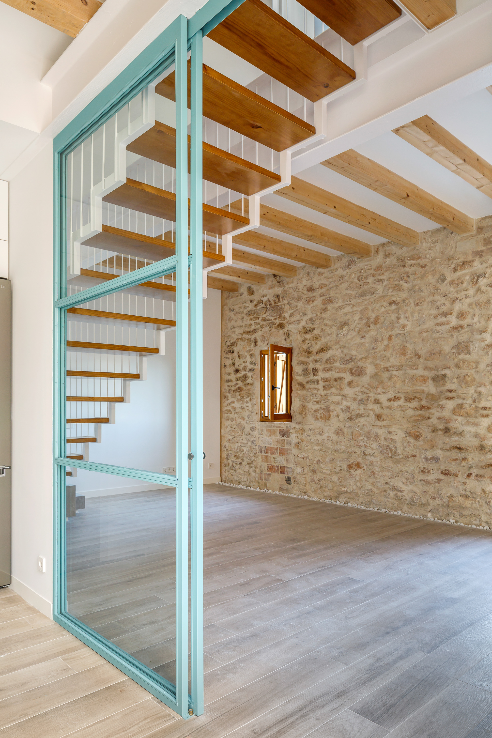 Open timber tread staircase with green steel frame against a limestone wall with narrow window opening