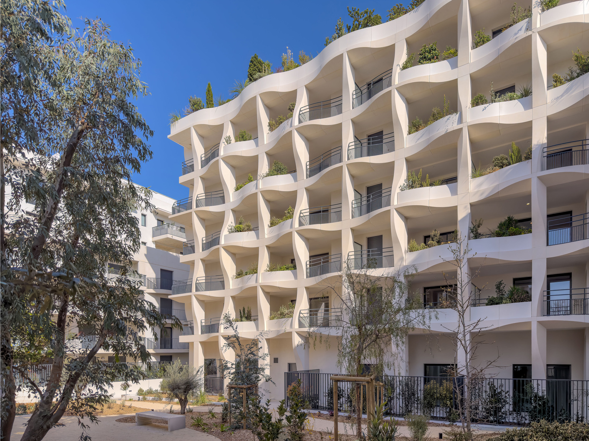 White concrete facade with wavy balcony edges and planters beneath a clear blue sky