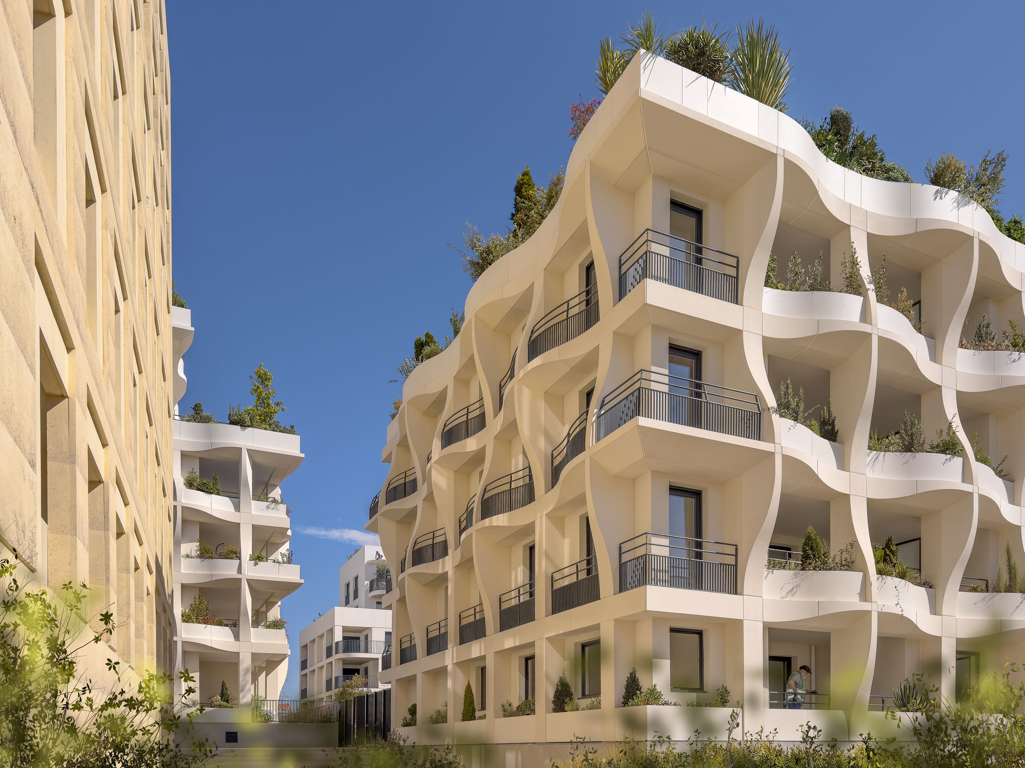 Courtyard view of the undulating white balconies with planted terraces under clear blue sky