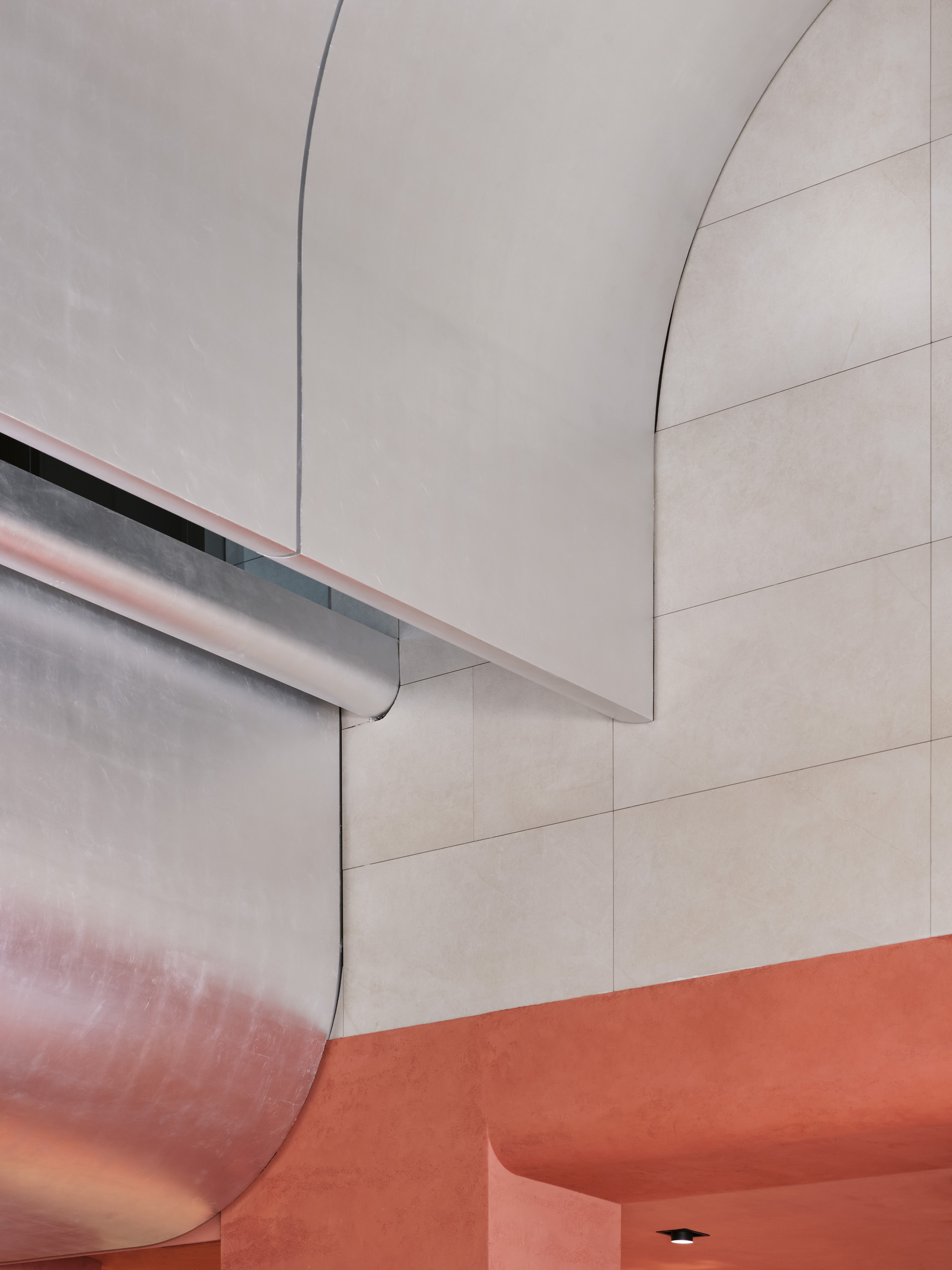 Detail of curved plaster wall forms with recessed lighting meeting an orange resin floor