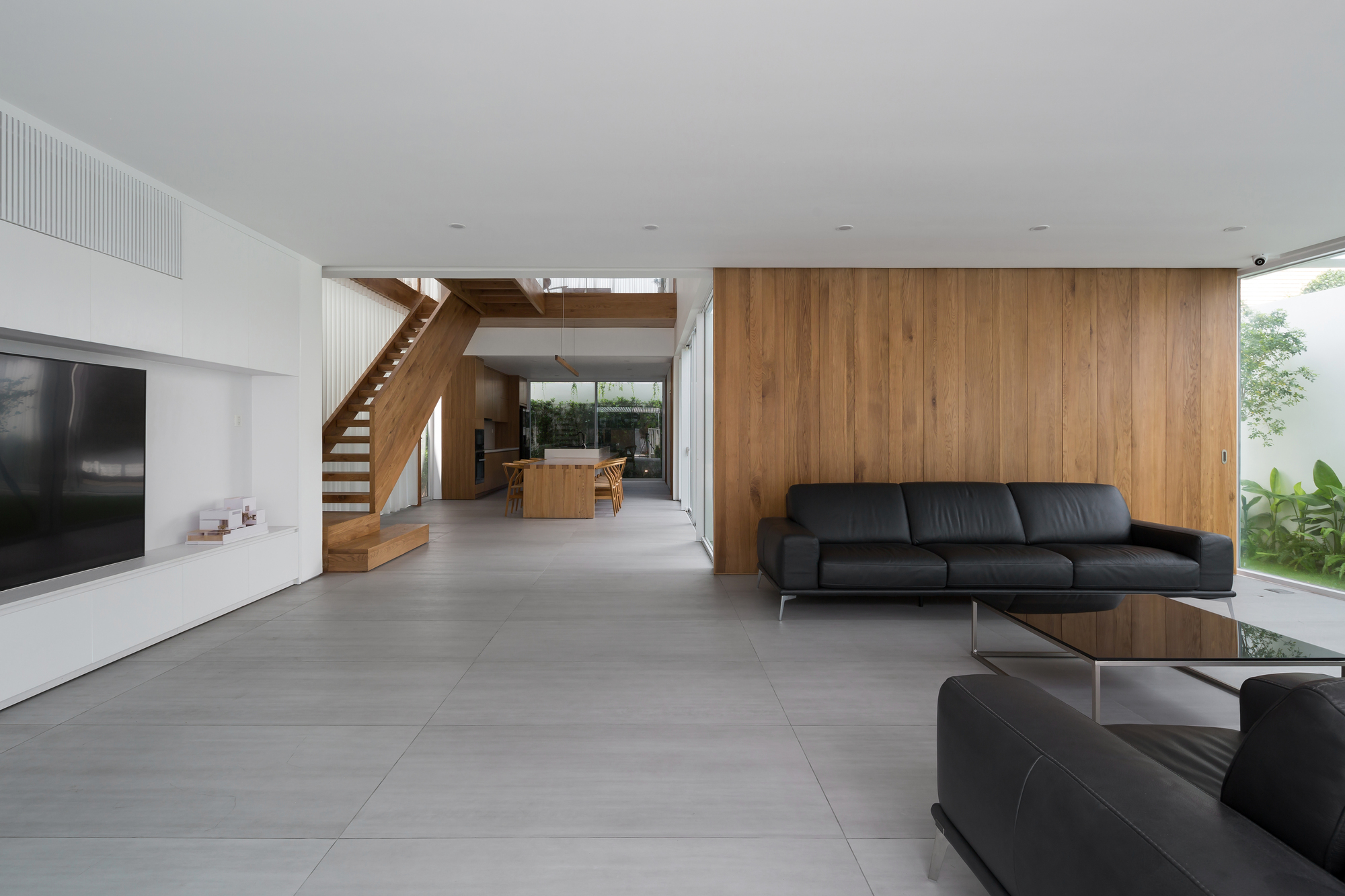 Double-height living room with timber staircase and large-format grey floor tiles beneath a white ceiling