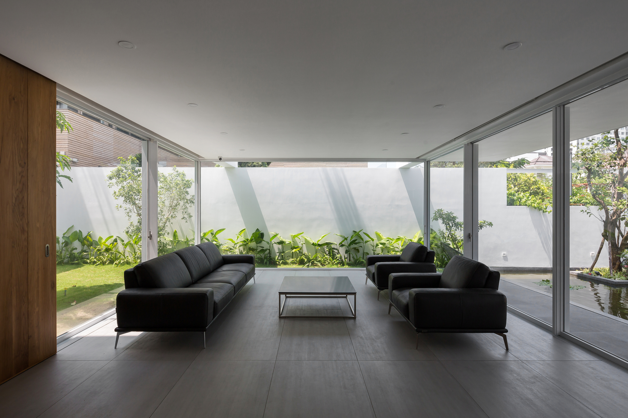 Living room with floor-to-ceiling glazing overlooking planted courtyard garden under overcast sky