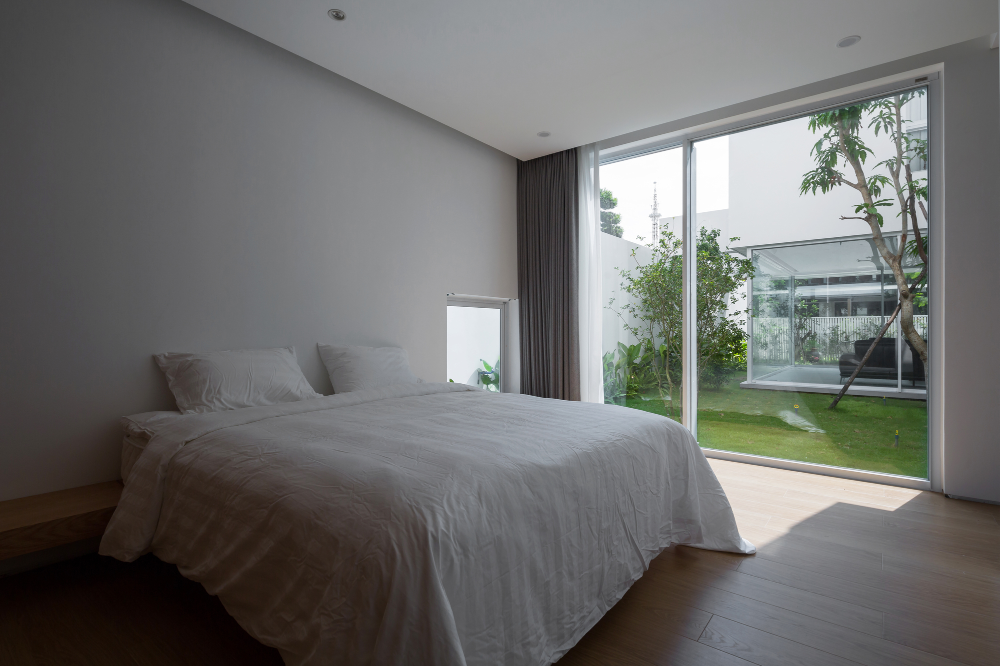 Bedroom interior with sliding glass wall overlooking an interior courtyard garden with lawn and trees