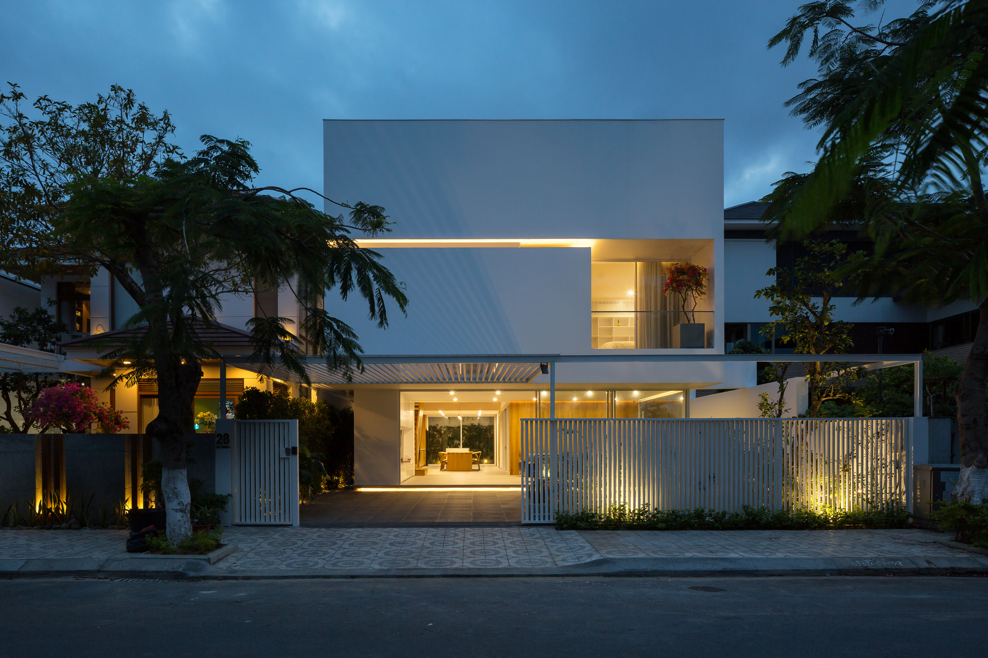 Street facade at twilight showing vertical slatted fence, recessed carport, and illuminated upper balcony