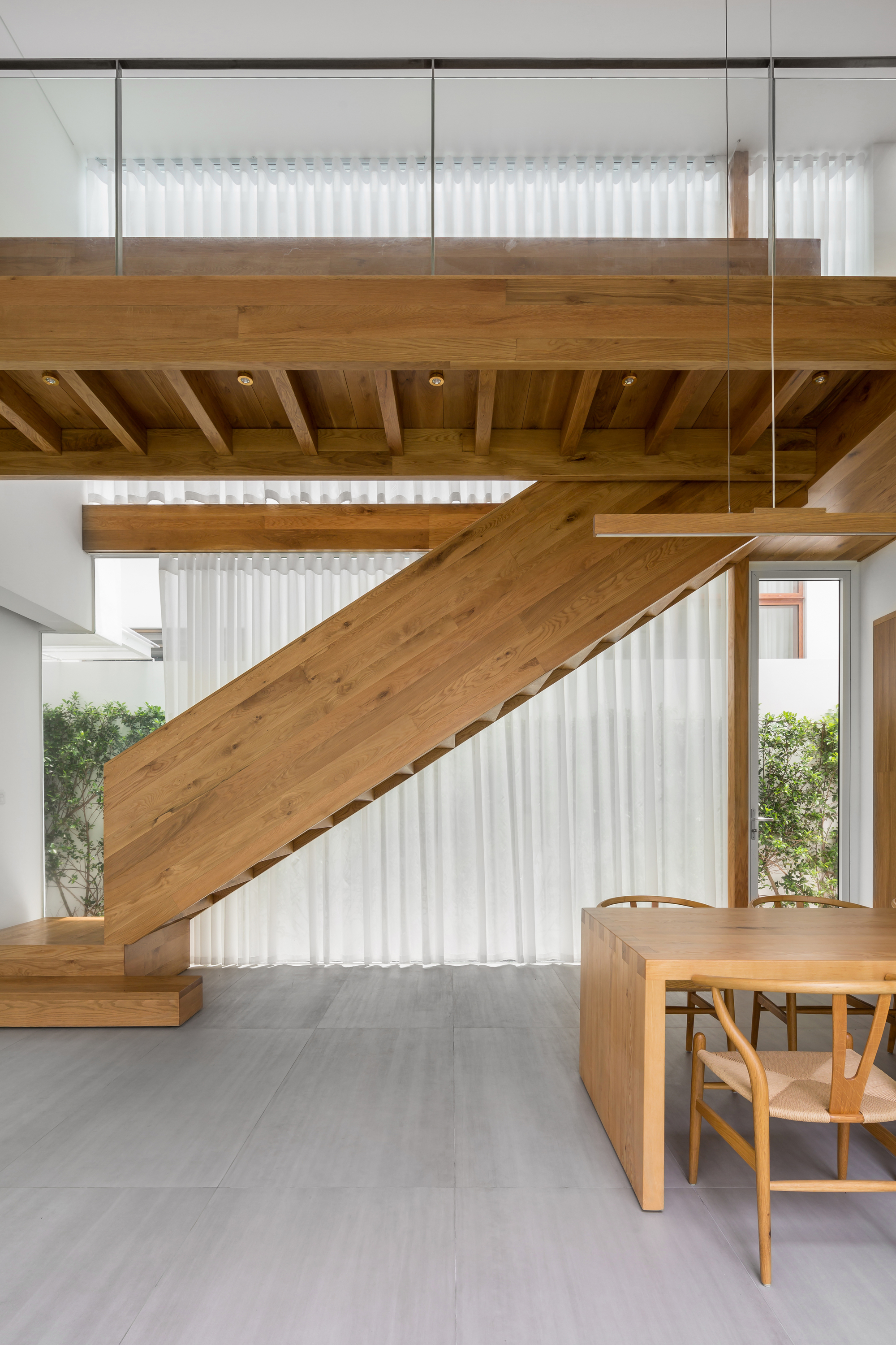 Timber staircase with exposed joists beneath the upper landing and white curtains filtering daylight