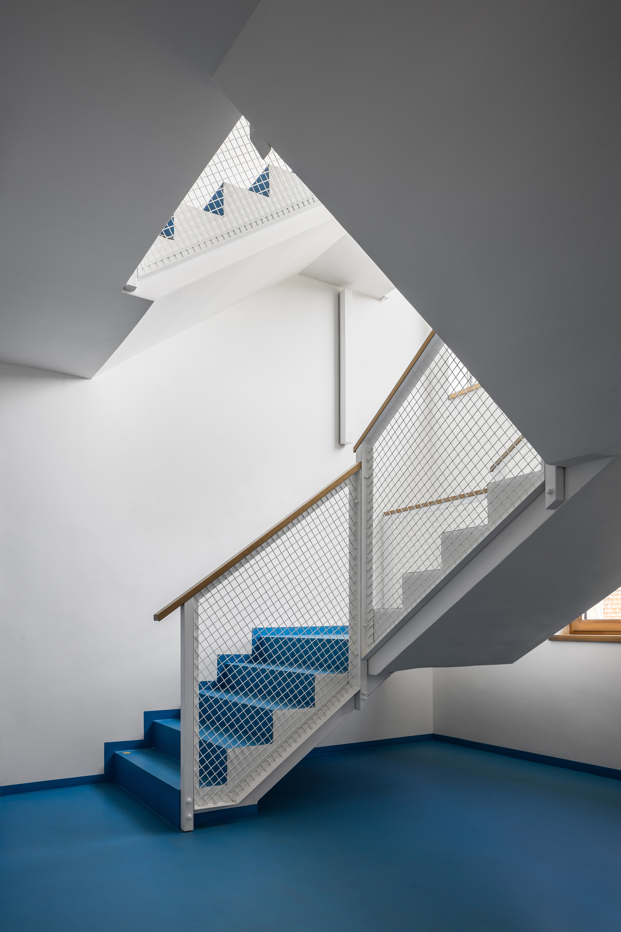 Interior staircase with blue treads and mesh infill under a peaked skylight