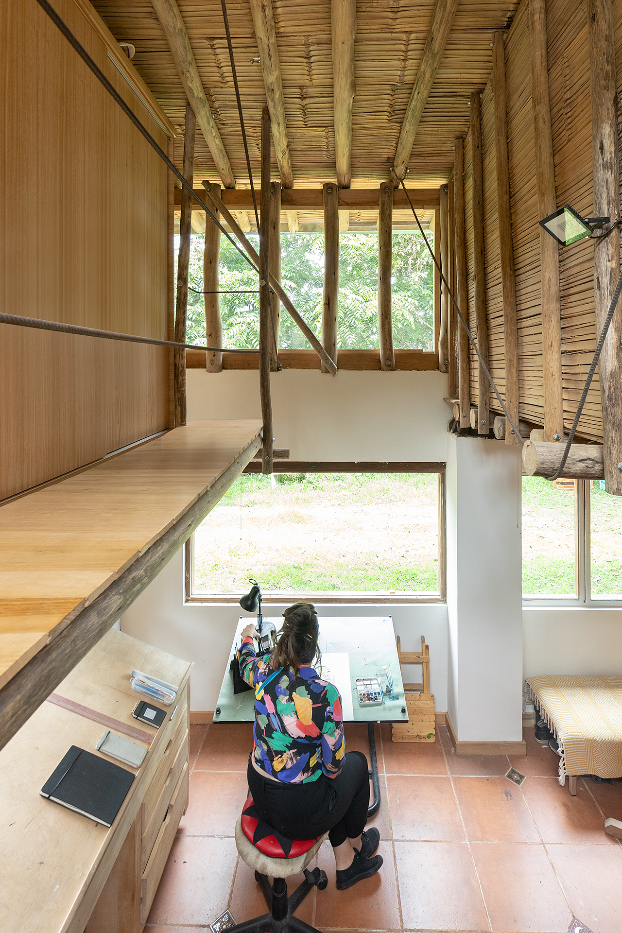 View from mezzanine workspace showing person at desk with horizontal window framing garden beyond