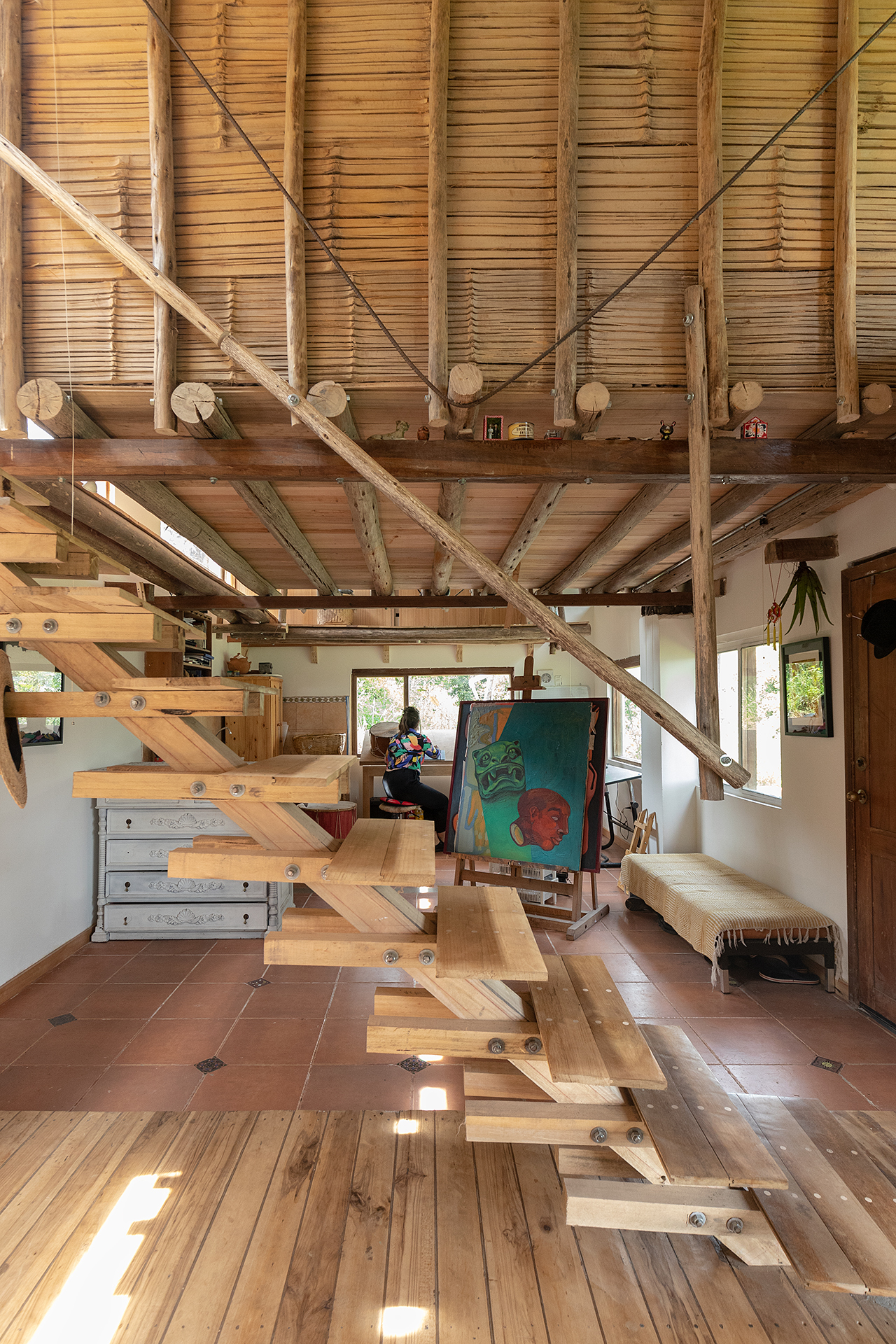 Open timber staircase beneath exposed beams and bamboo ceiling with a person working at the far end