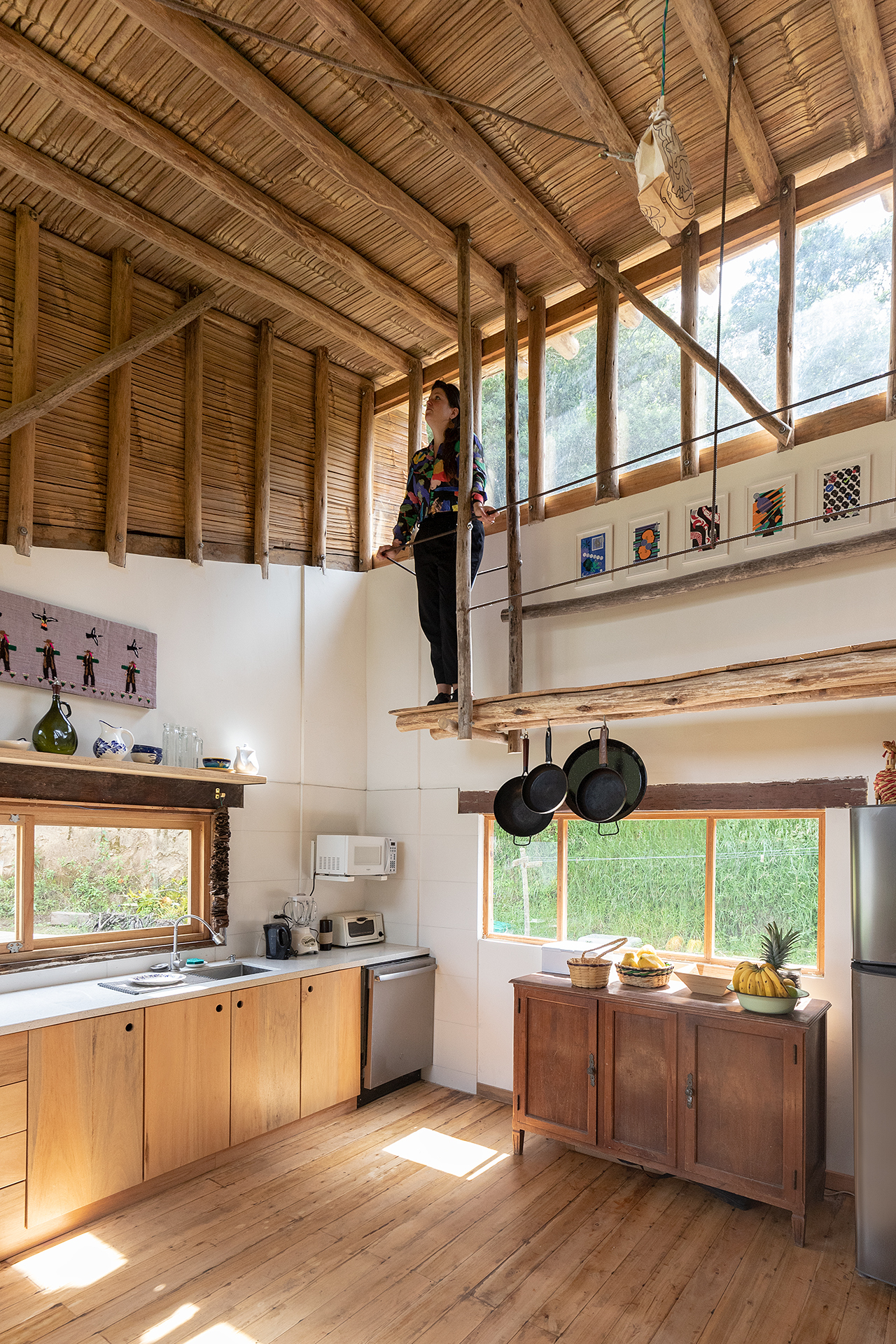 Double-height kitchen space with bamboo slat ceiling, timber beams, and a person standing on a mezzanine platform