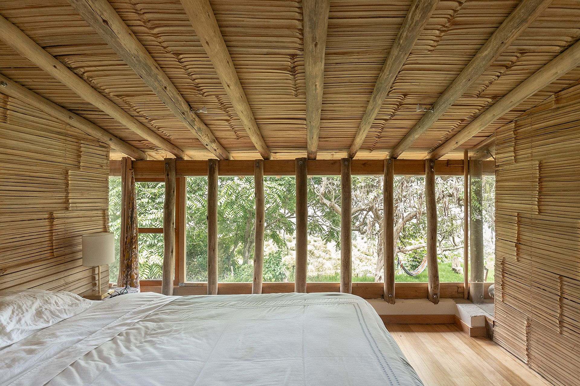 Bedroom with bamboo slat ceiling and walls, floor-to-ceiling glazed doors opening to greenery beyond