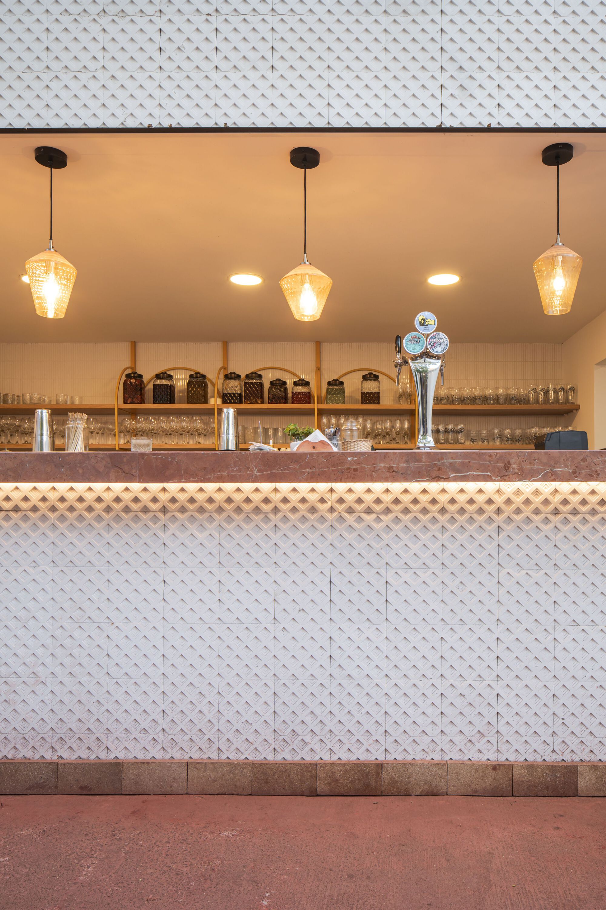 Bar counter with white diamond-patterned tile cladding and three amber pendant lights above