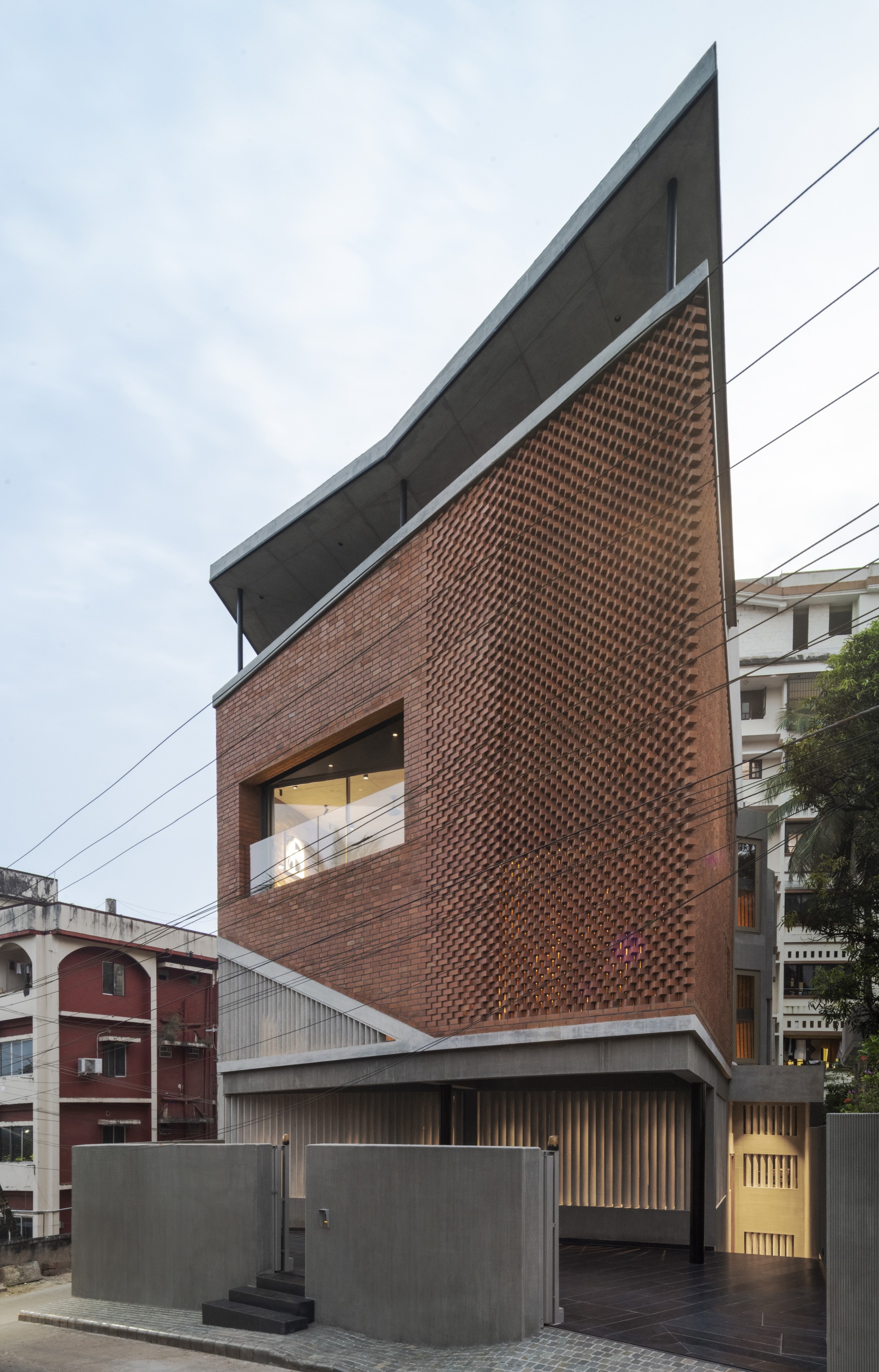 Sharp angular facade with projecting brick screen and cantilevered concrete roof slab at dusk