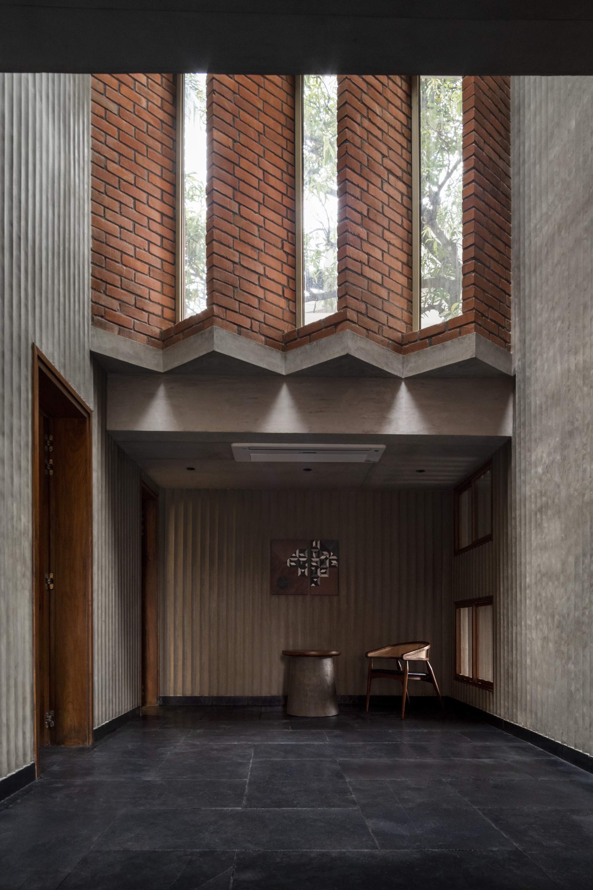 Double-height entry foyer with zigzag brick clerestory windows and concrete beams over dark stone flooring