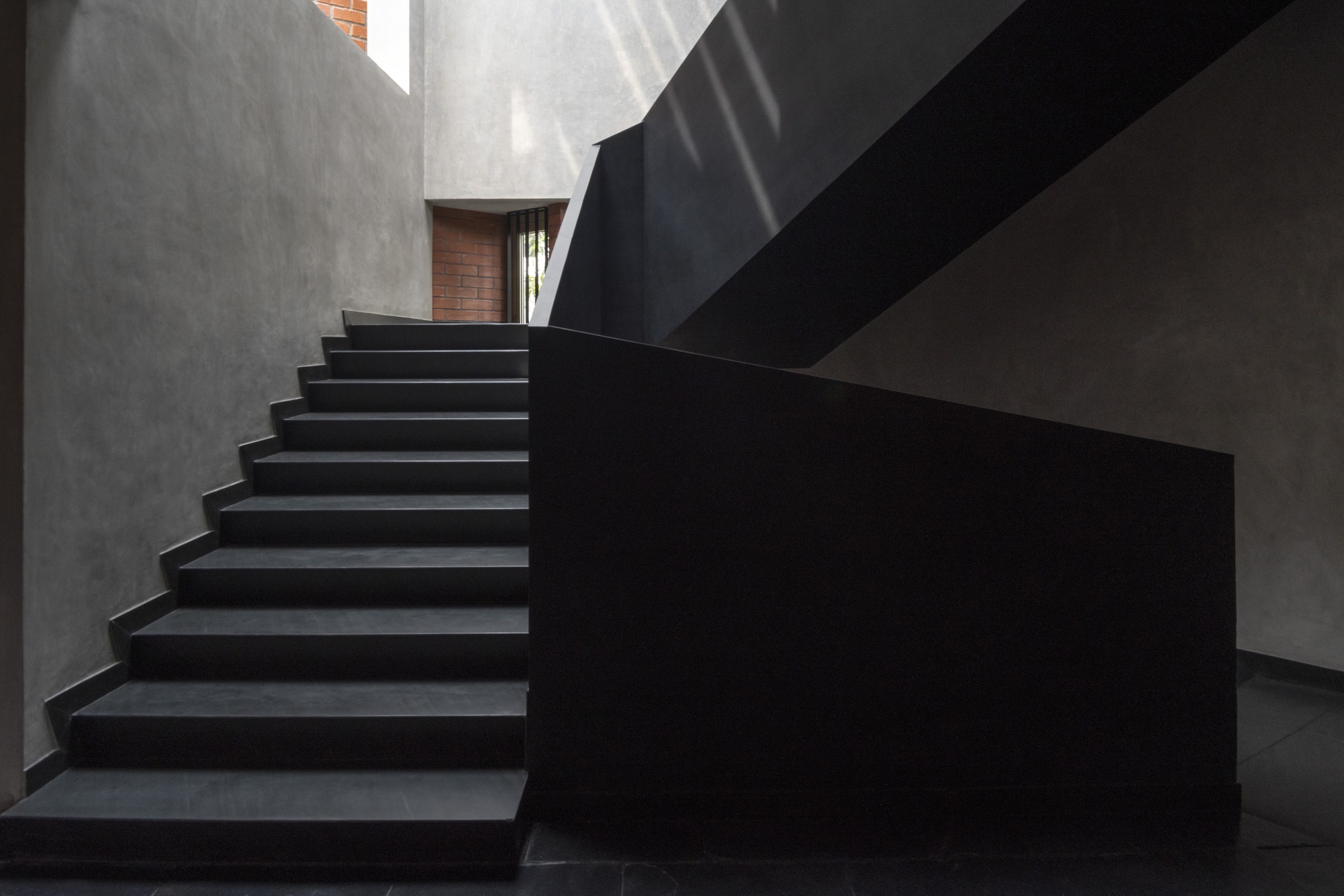 Black cantilevered staircase rising between grey concrete walls with diffused daylight from above
