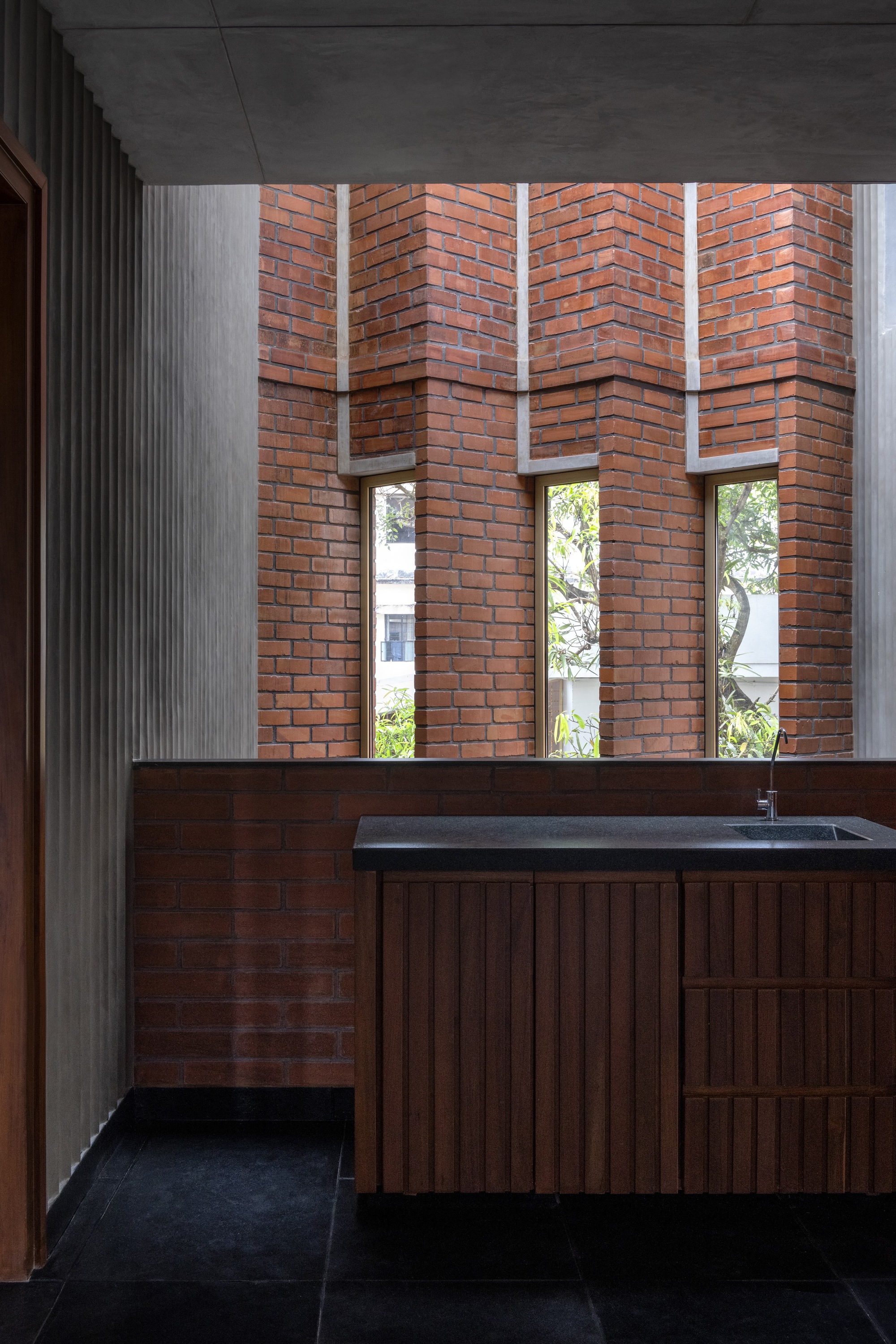 Bathroom vanity beneath herringbone patterned brick wall with vertical window slots framing greenery outside