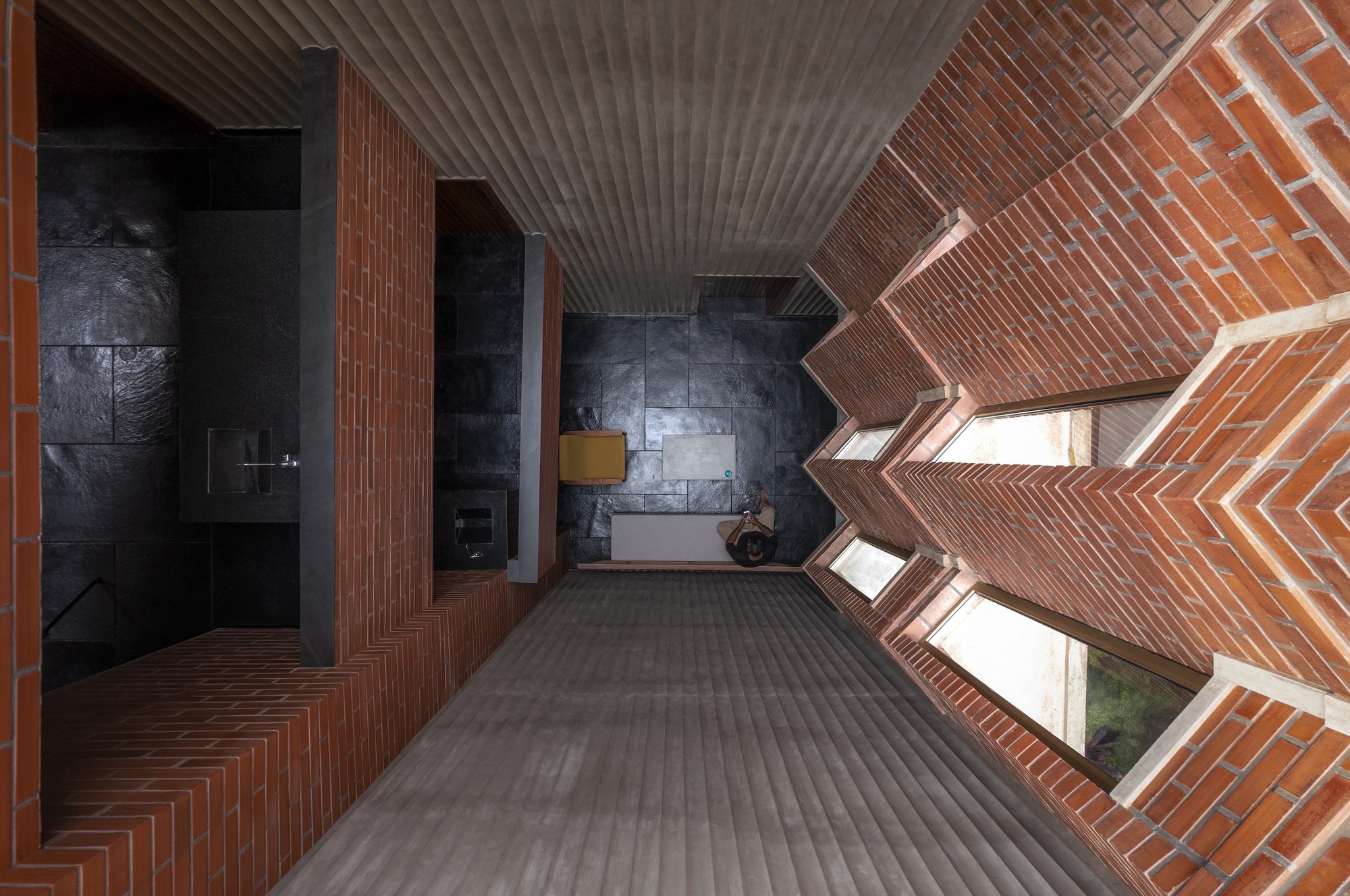 Interior corridor with zigzagging brick walls, clerestory windows, corrugated metal ceiling, and dark tile accent wall