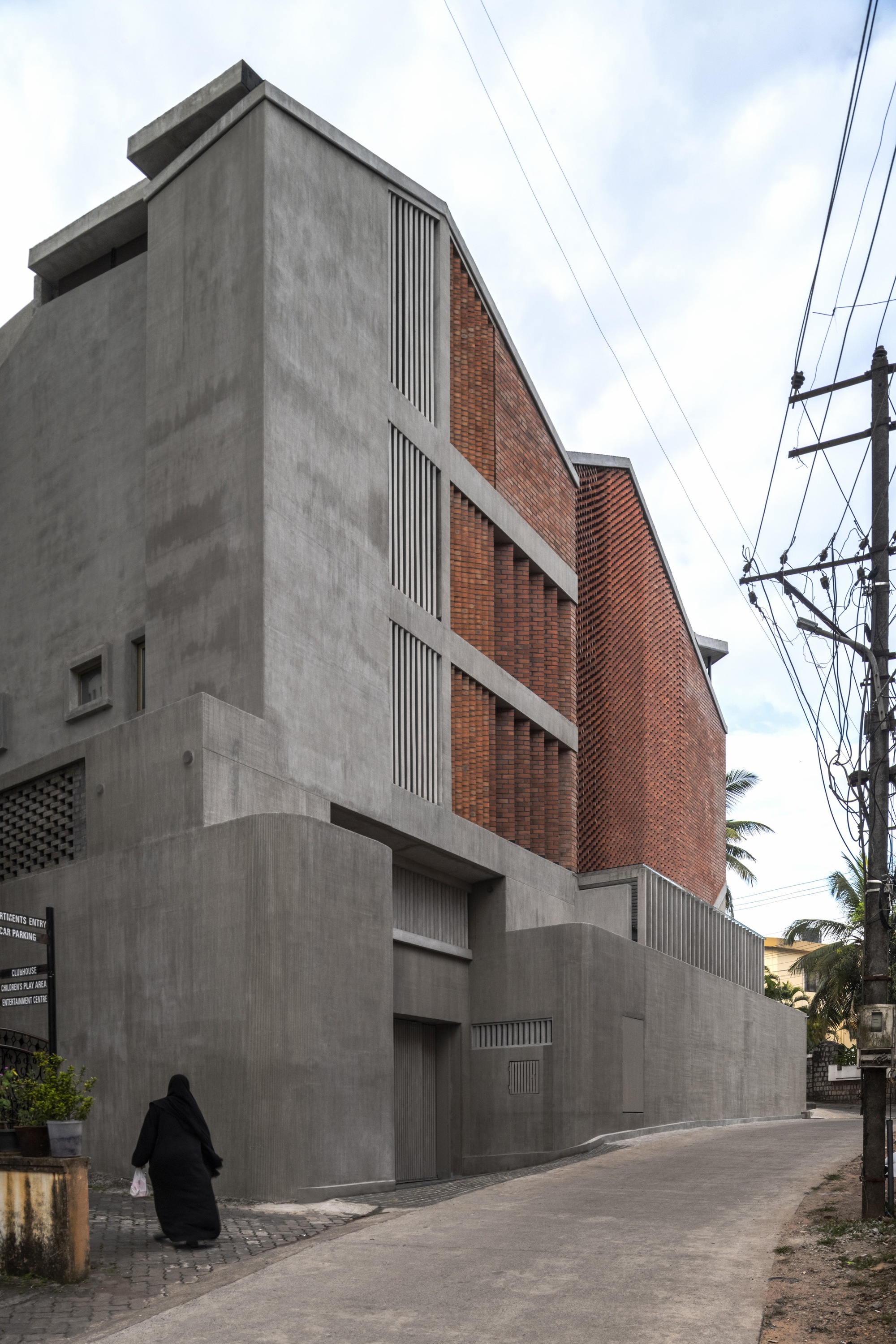 Street view of concrete and brick facade with vertical louvres and overhead power lines as a figure walks past