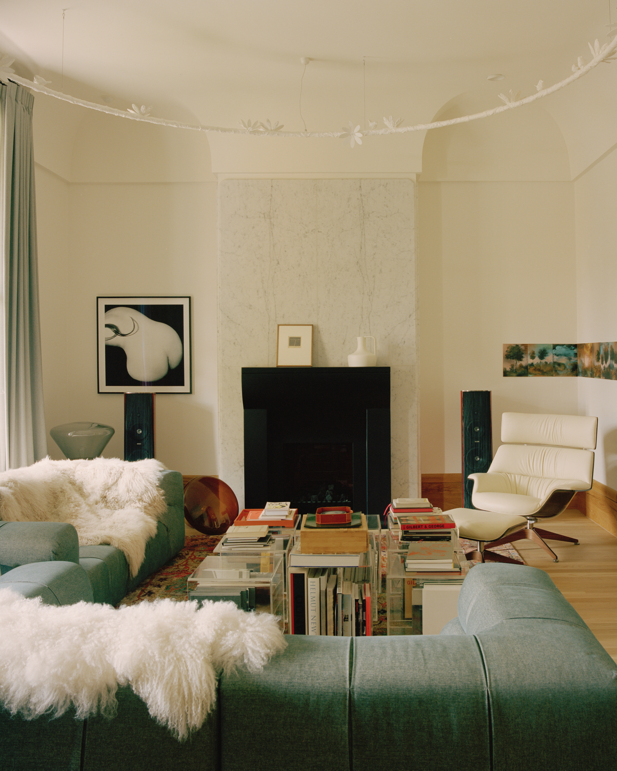 Living room with black fireplace surround, acrylic book tables and green sectional sofas with sheepskin throws