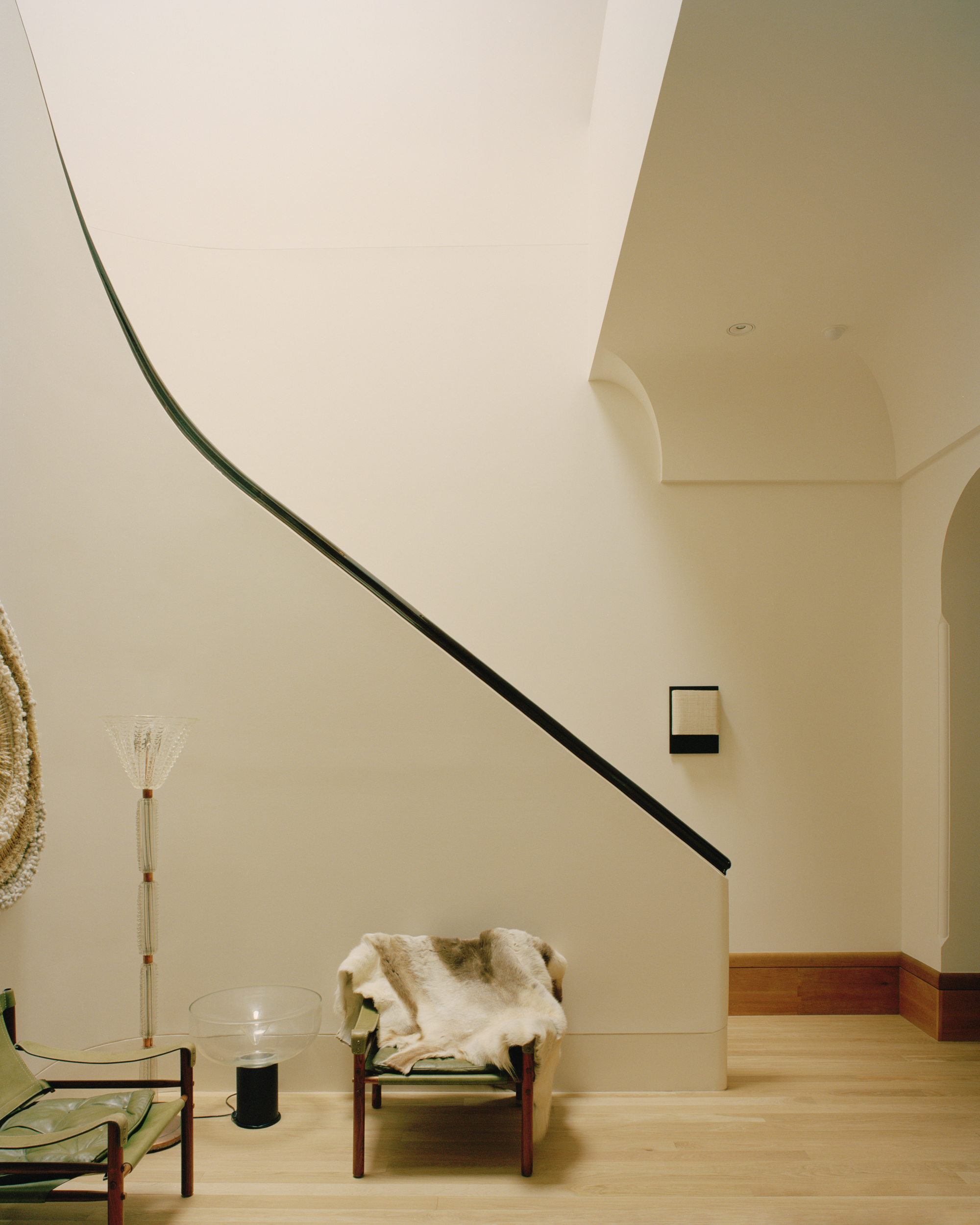 Curved staircase with black handrail ascending past pale walls and an arched opening in oak flooring