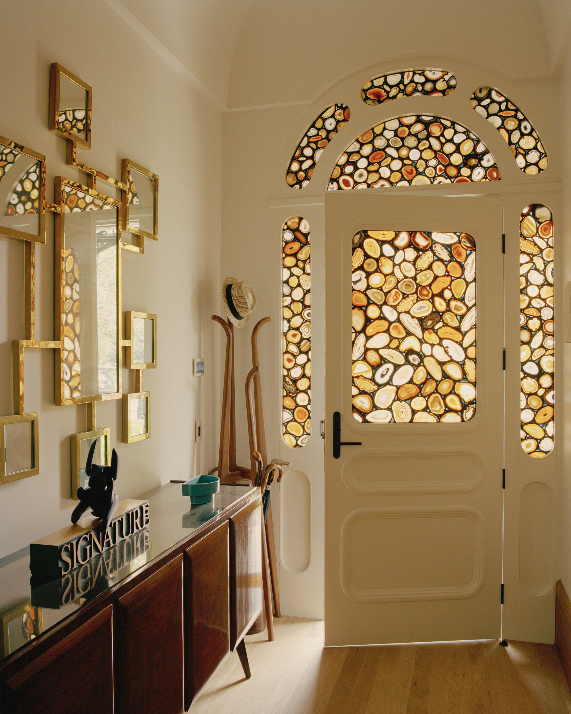 Arched entry door with backlit agate stone panels set into timber framing beside brass wall shelving