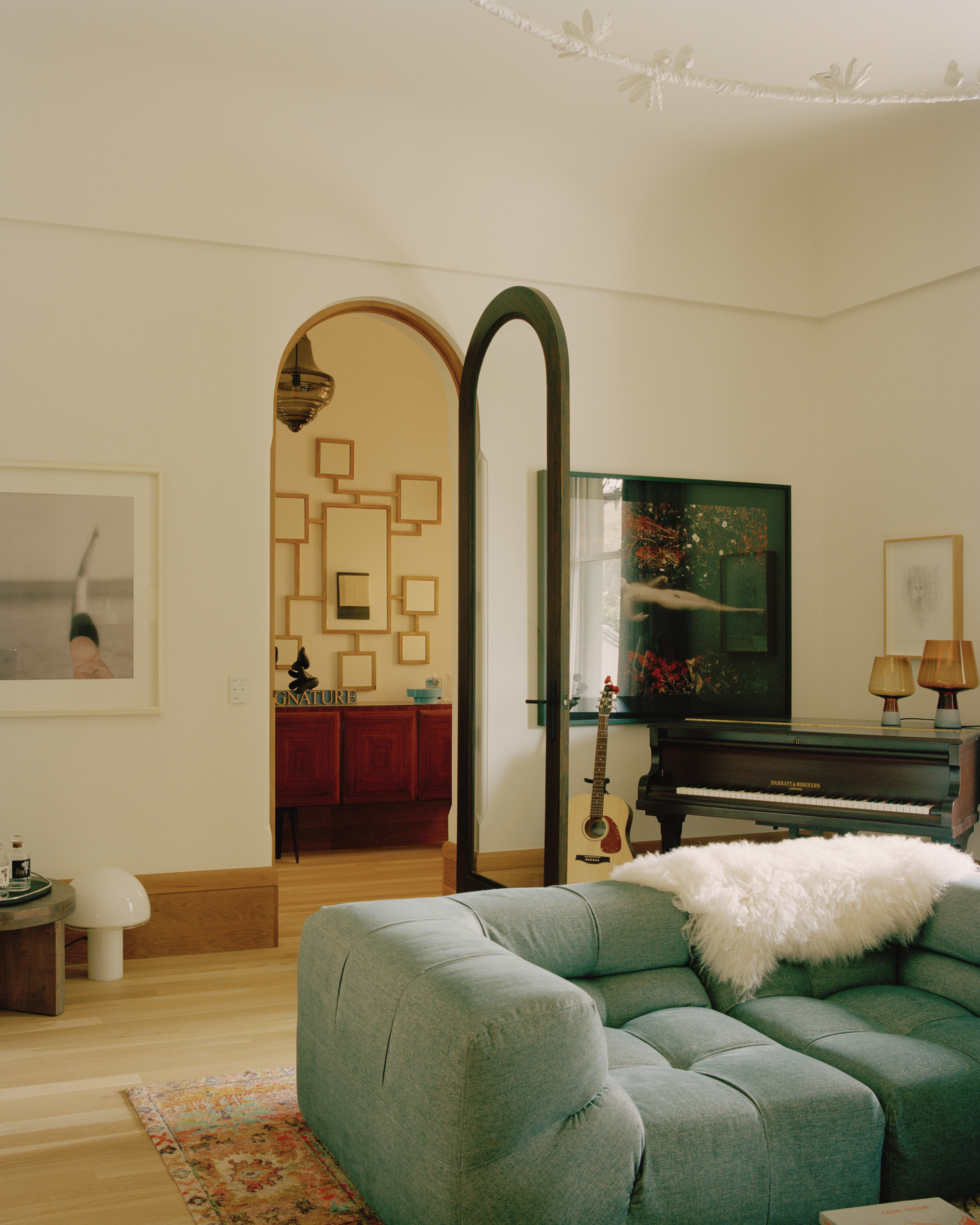 Living room with arched doorway framing a view through to an adjacent room with piano and artwork