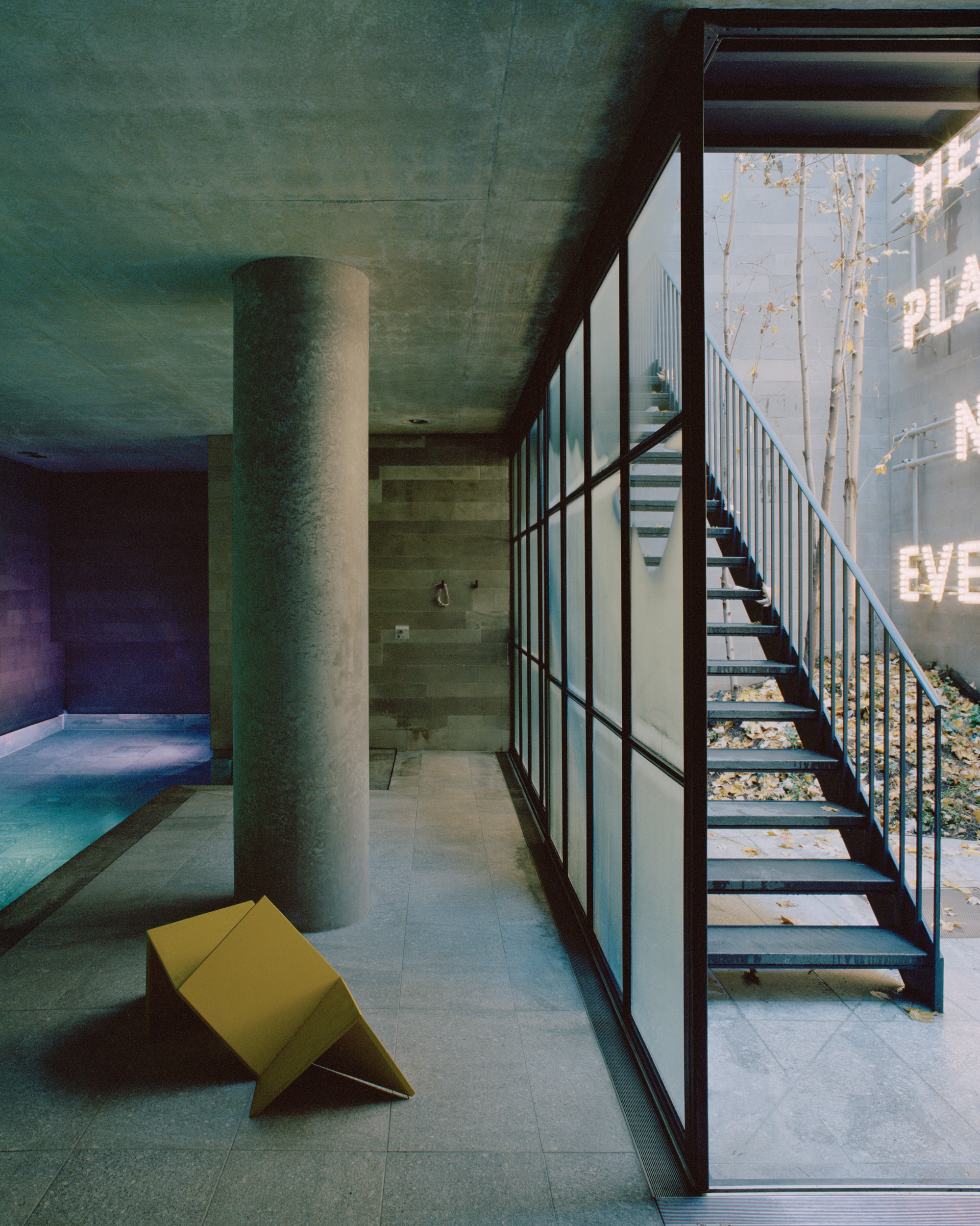 Open steel staircase beside floor-to-ceiling gridded window wall overlooking trees in daylight