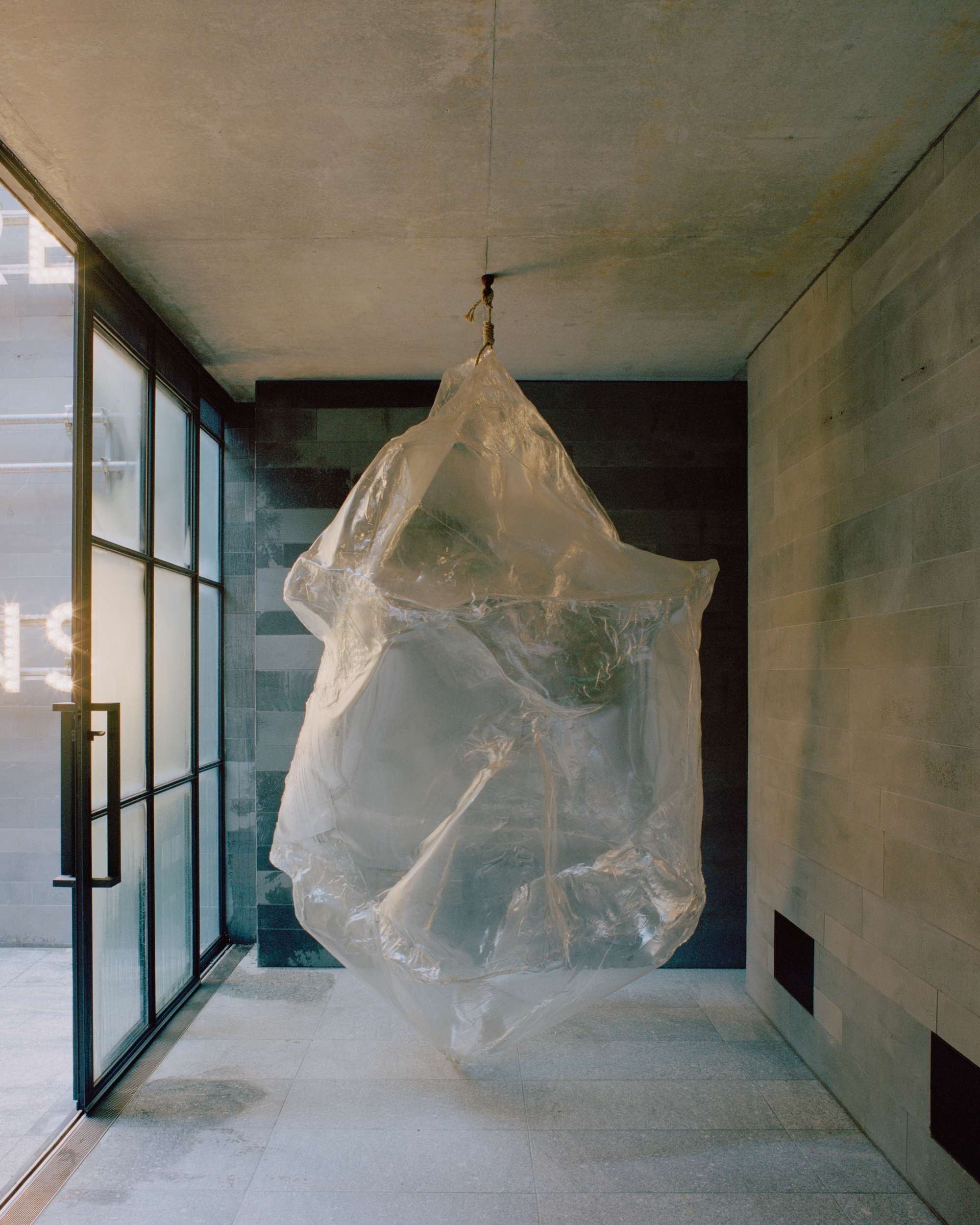 Interior hallway with suspended translucent sculpture beside glazed wall and board-formed concrete surfaces