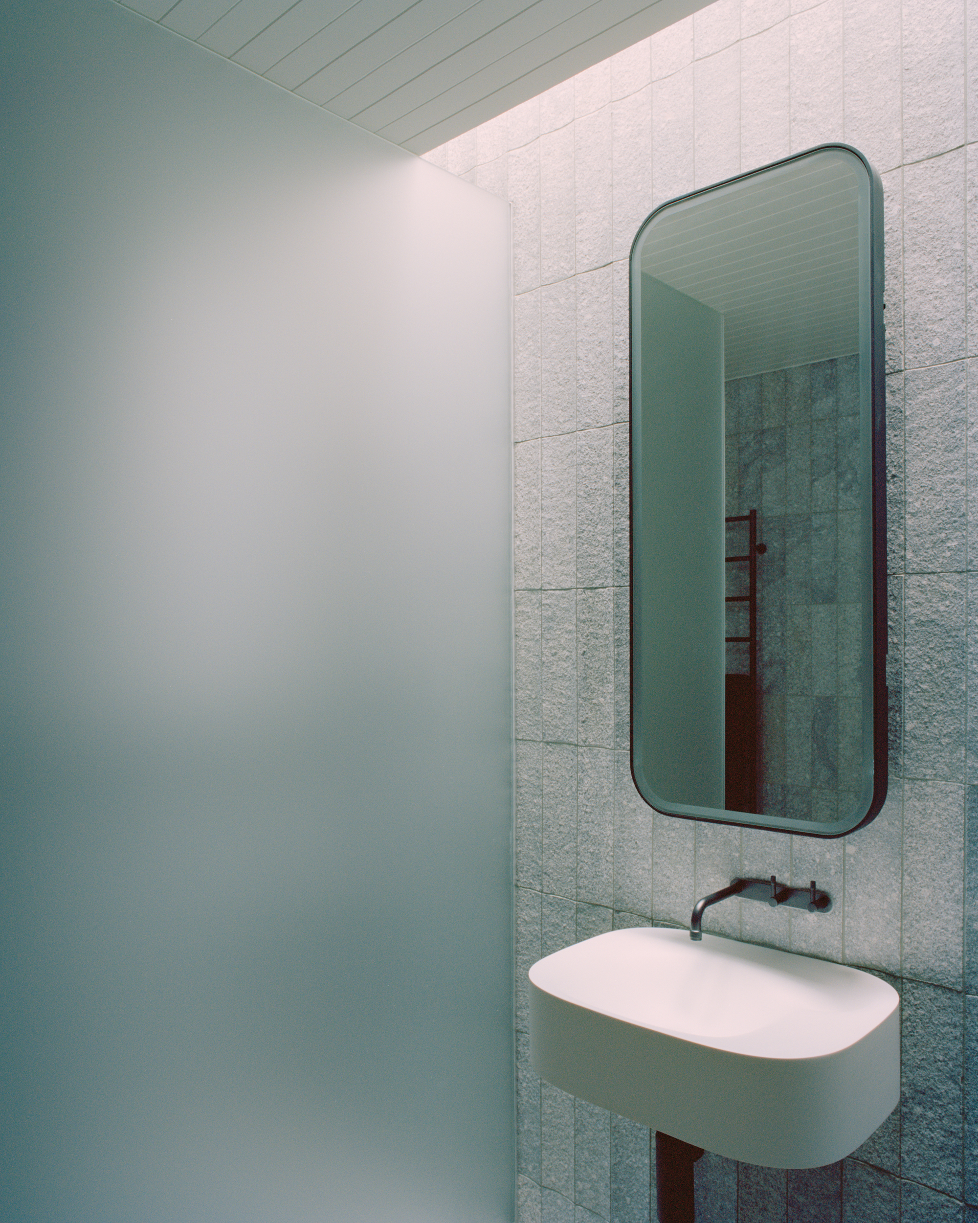 Bathroom corner with rounded mirror above floating sink and pale green tile cladding