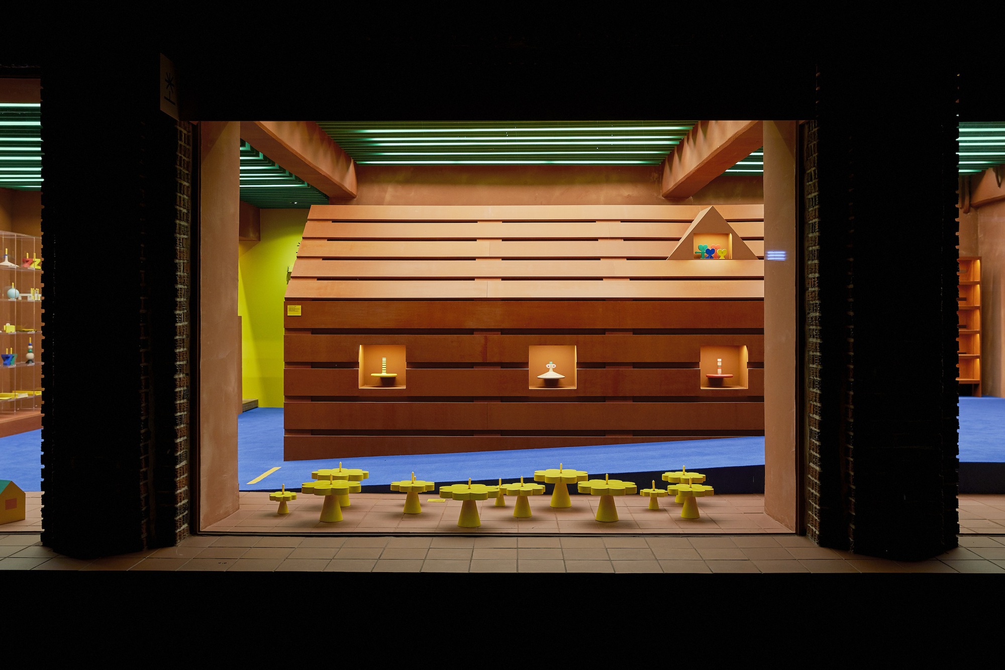 Horizontal wood-clad volume with square window cutouts and candles, flanked by black brick columns at night
