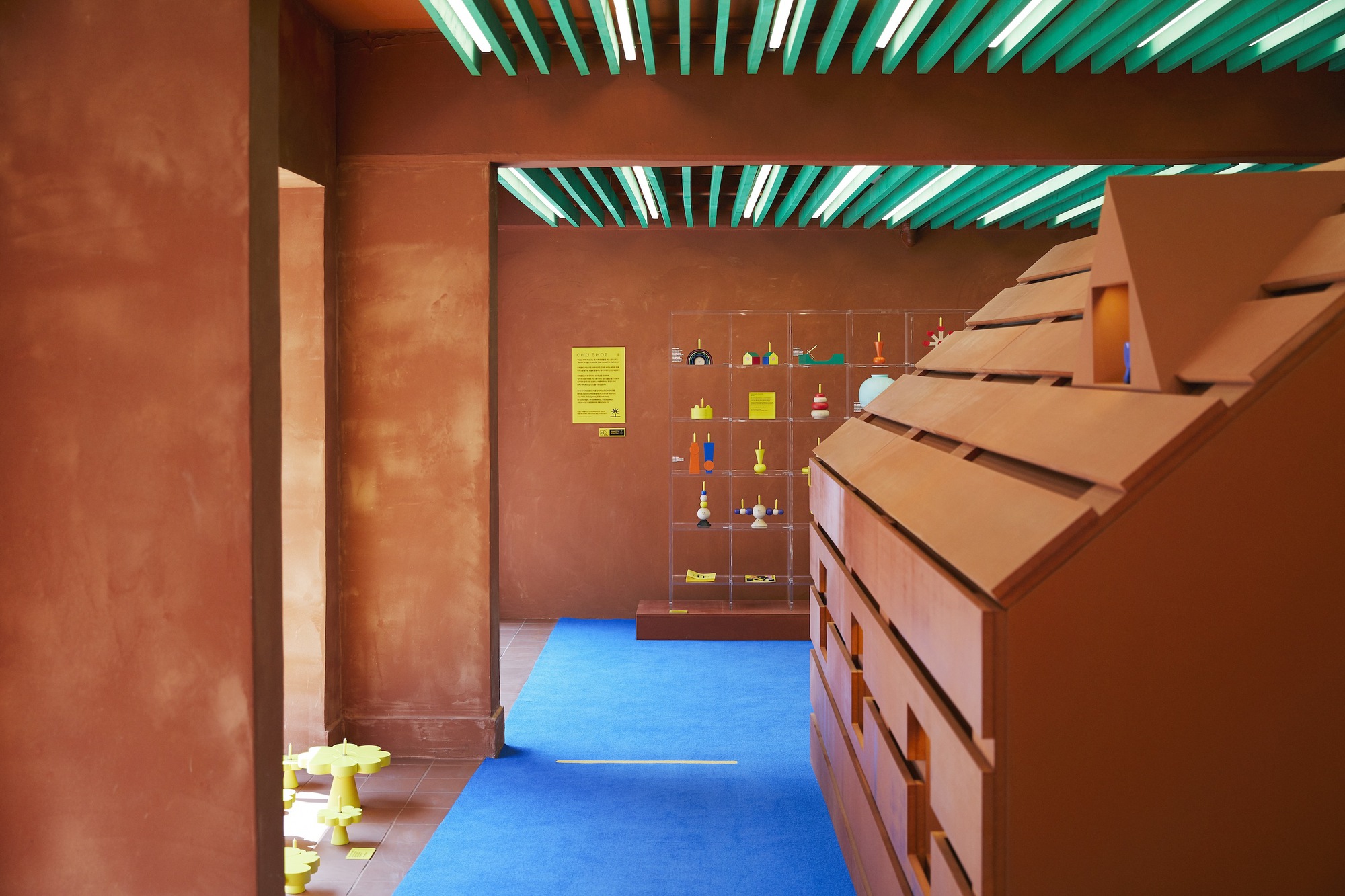 Interior passageway with ochre plastered walls, angled timber stair, and green ceiling slats filtering daylight