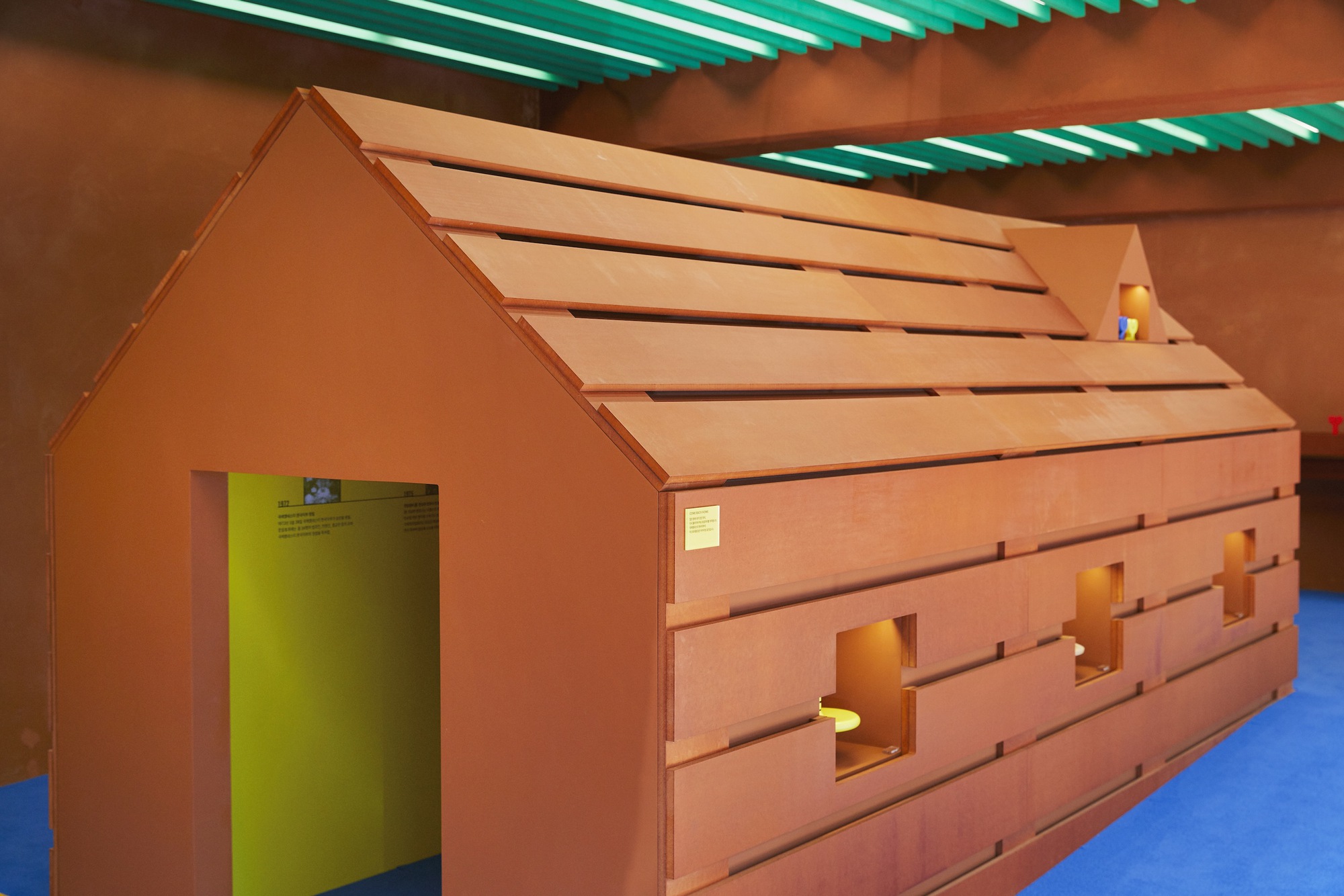House-shaped installation with layered timber cladding and doorway revealing lime green interior